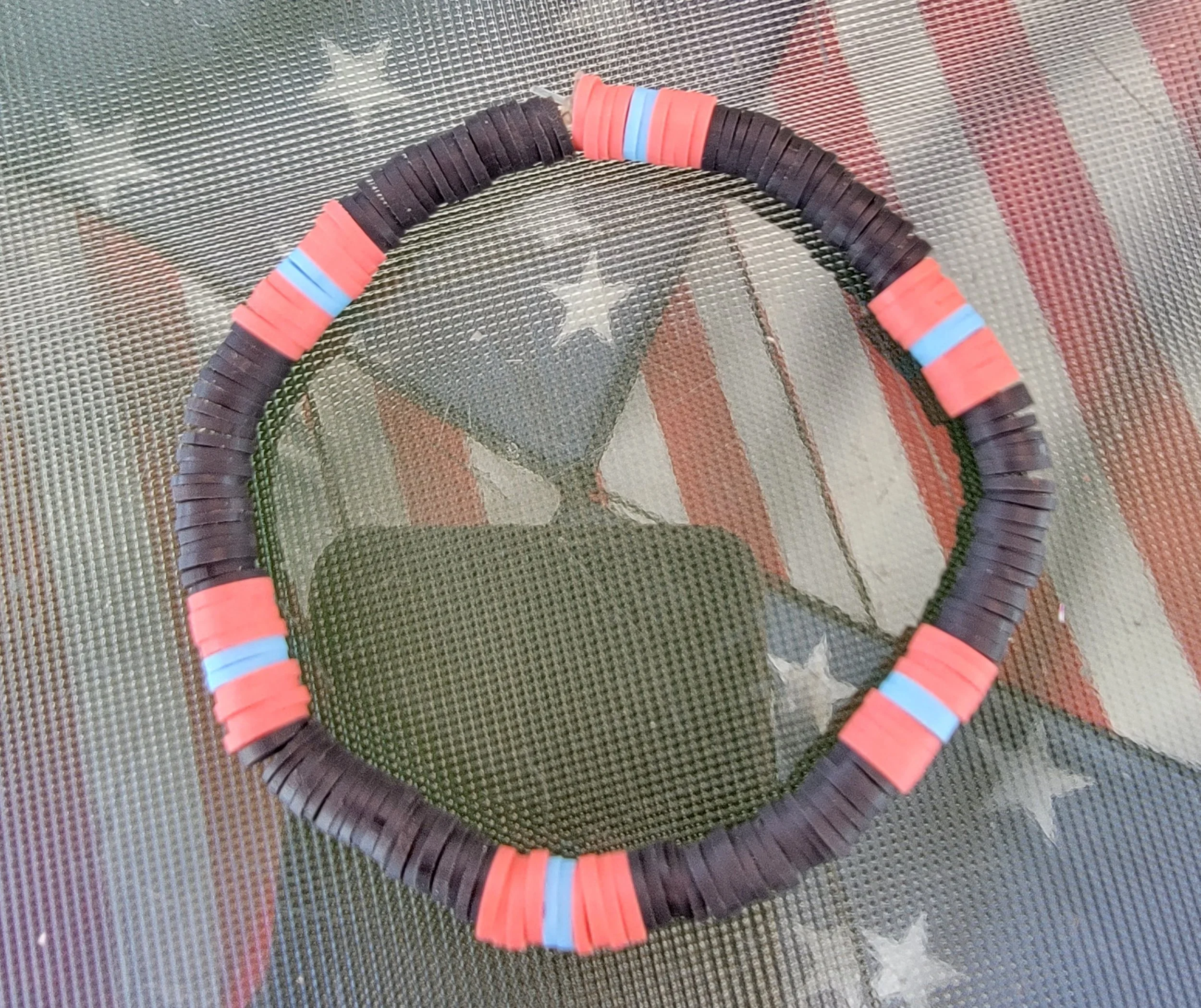 A tennis racket frame with red and black plastic pieces, blue accents, and a background of an American flag with stars and stripes.
