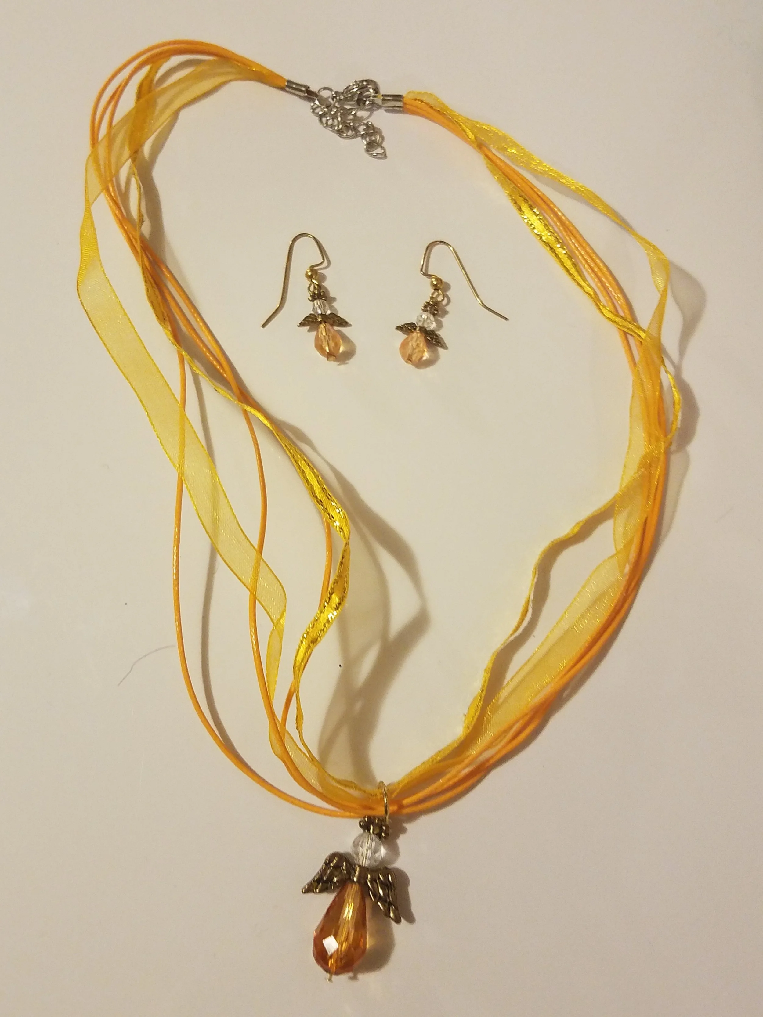 Yellow and orange layered ribbon necklace with angel pendant and matching dangling earrings with orange gemstone and leaf accents.