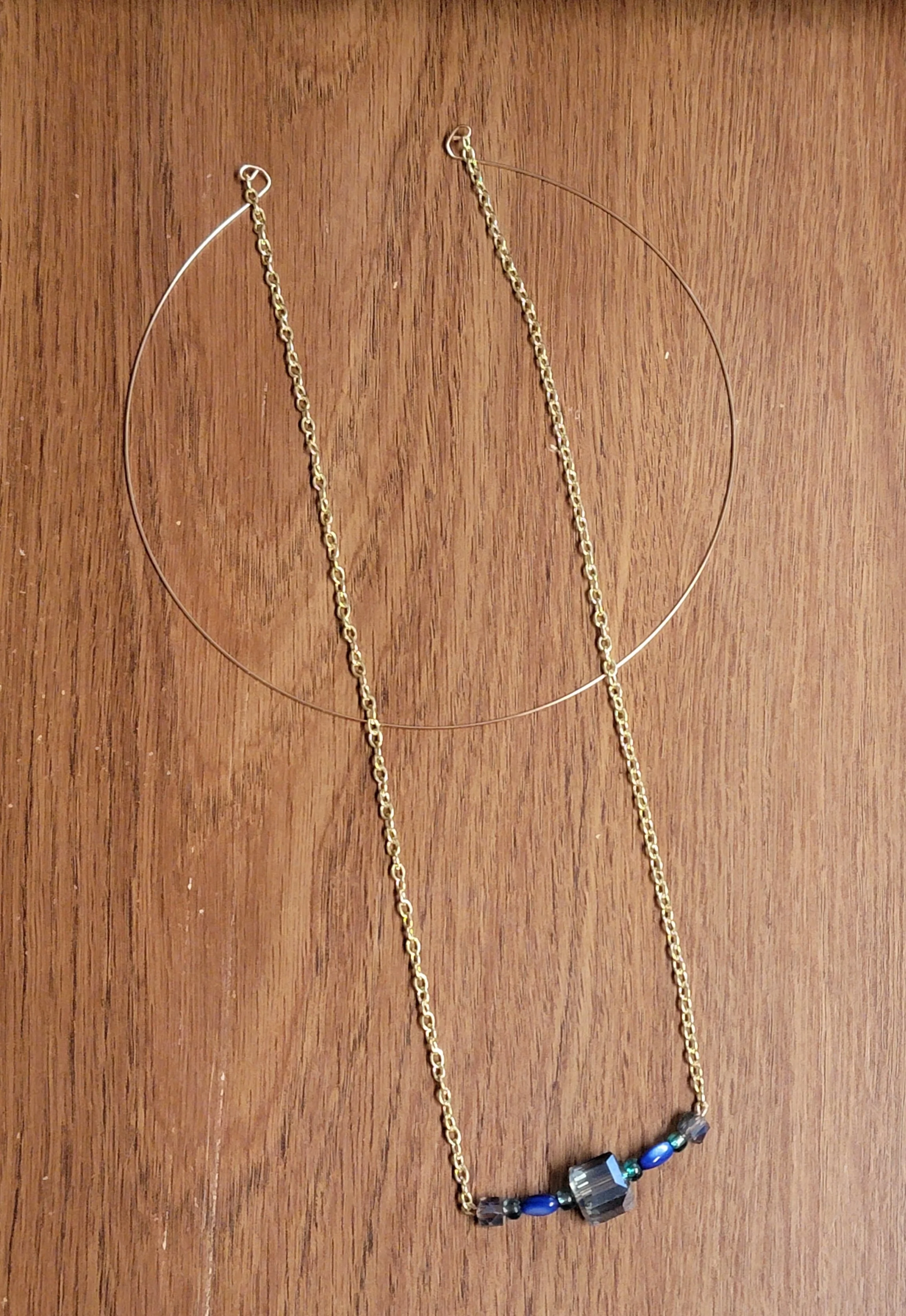 Gold chain necklace with black, blue, and clear beads, placed on a wooden surface.