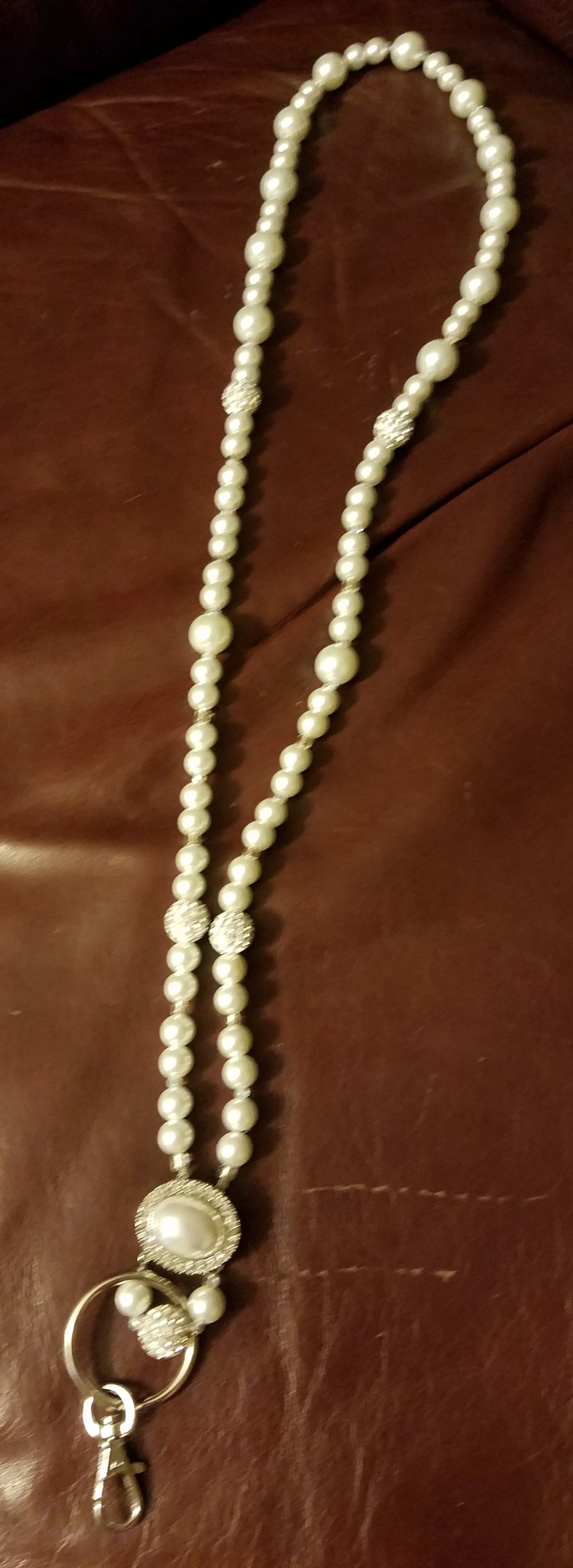 A pearl necklace with a decorative clasp and charm, displayed on a brown surface.