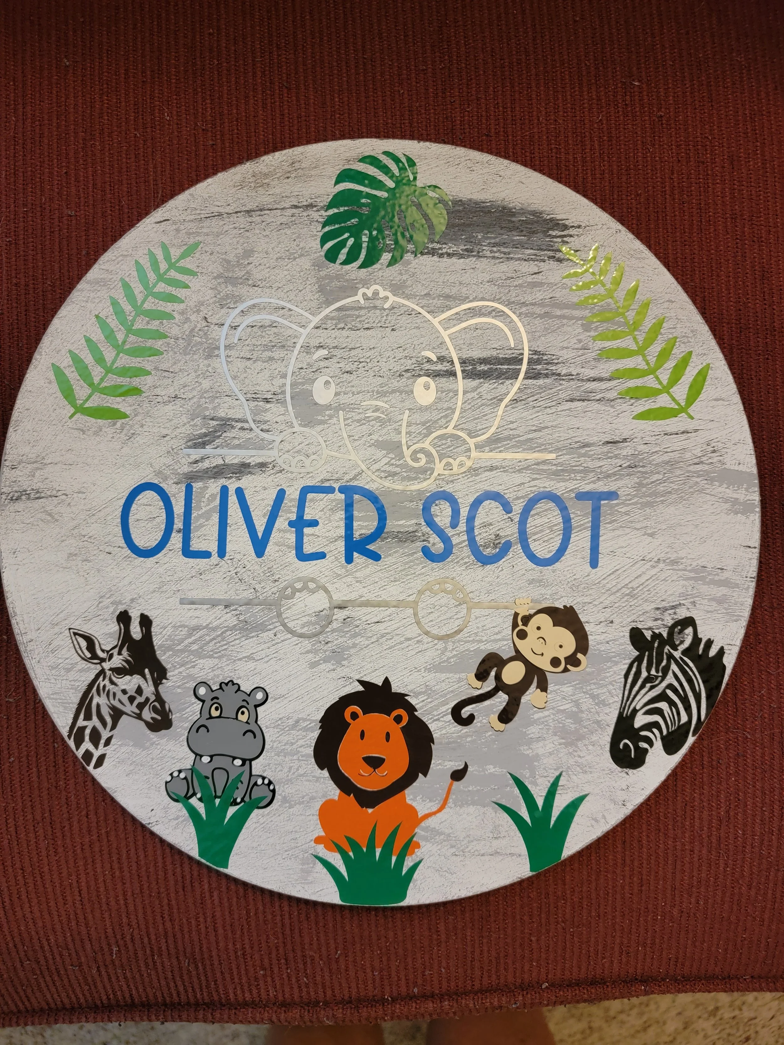 Decorative sign featuring a cartoon lion, monkey, zebra, giraffe, and leaves, with the text 'Oliver Scot'