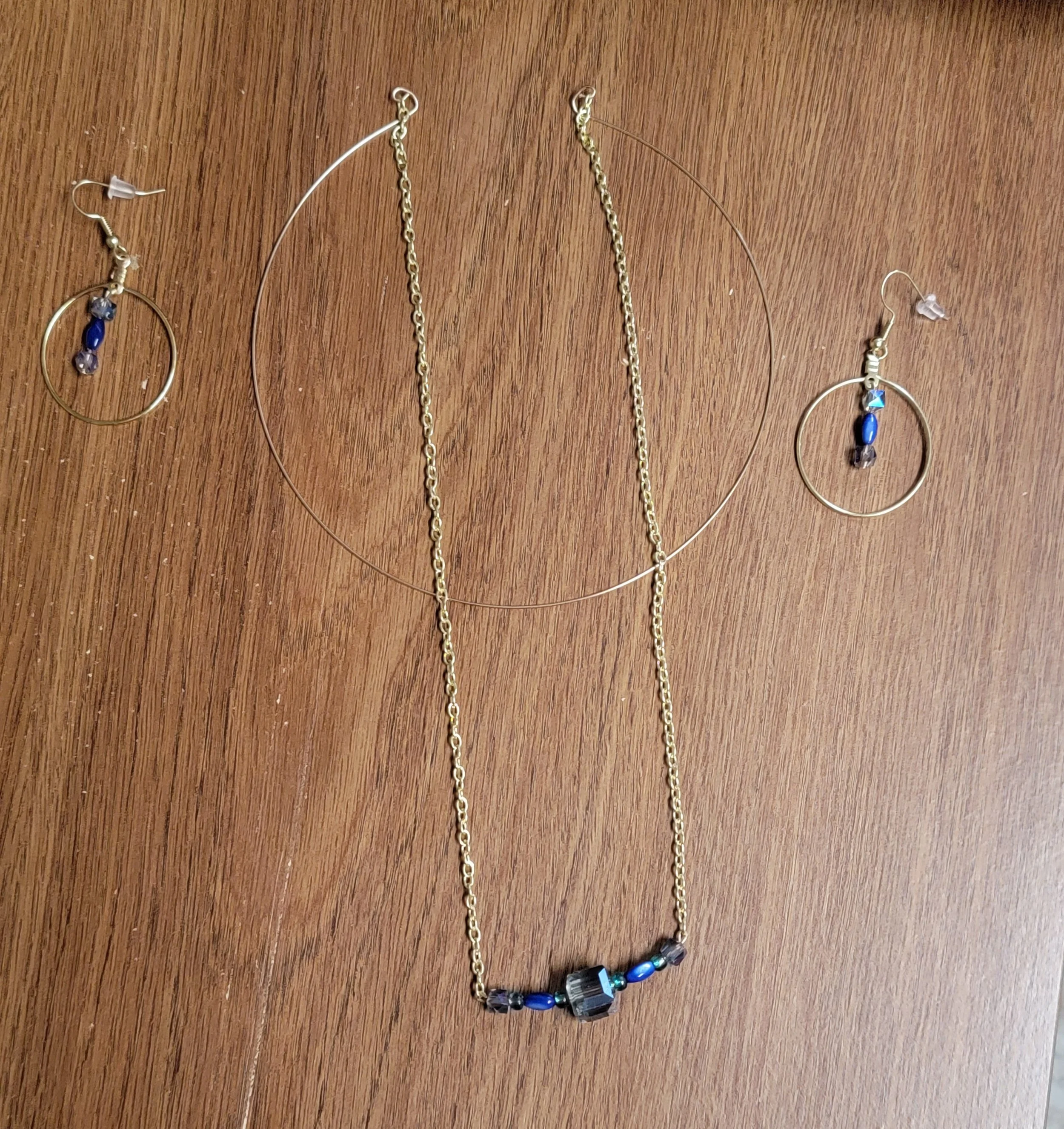 Gold jewelry set including a necklace and matching earrings with blue and dark beads on a wooden surface.