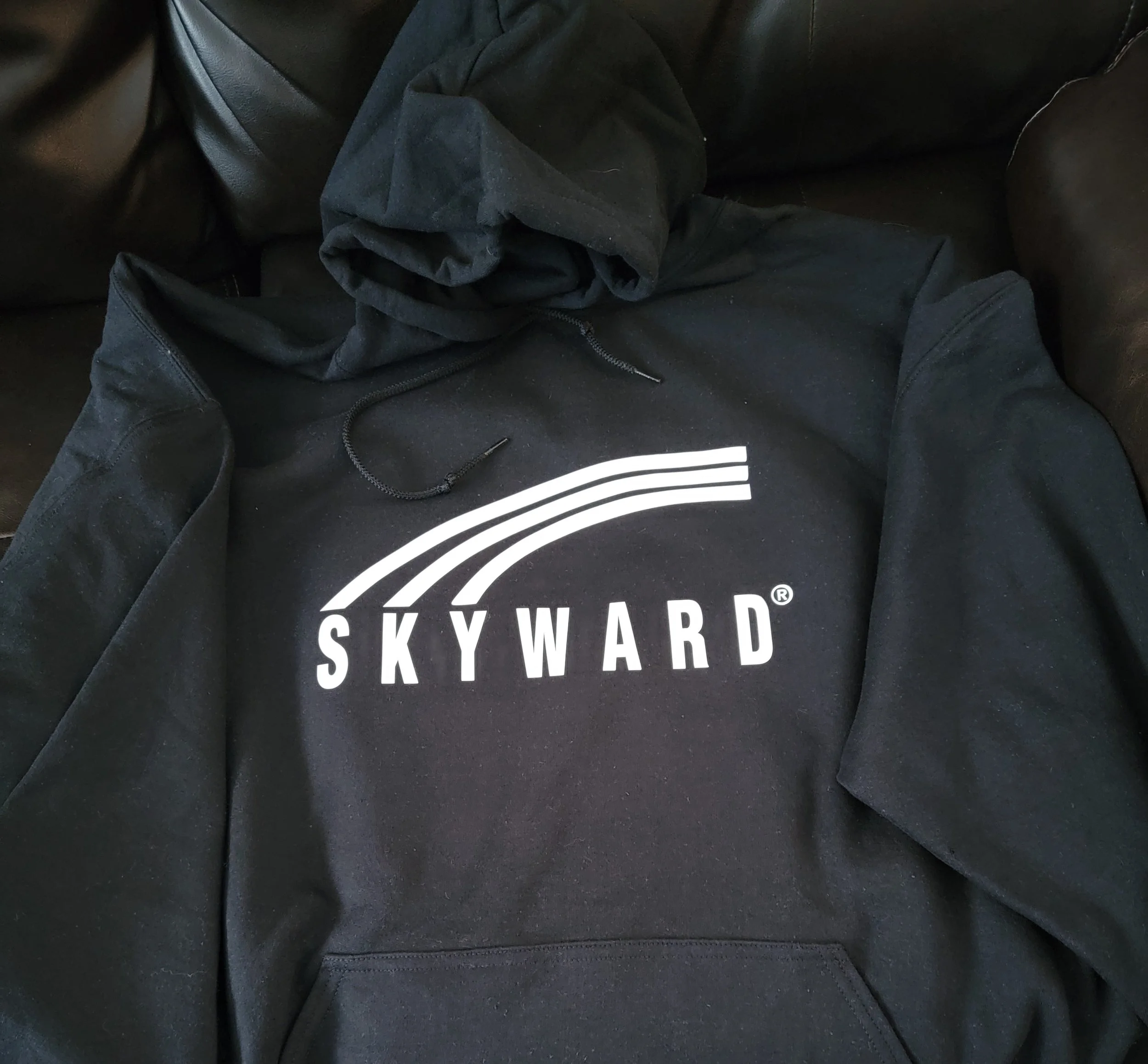 Black hoodie with a white Skyward logo on the front, placed on a black surface with the hood up.