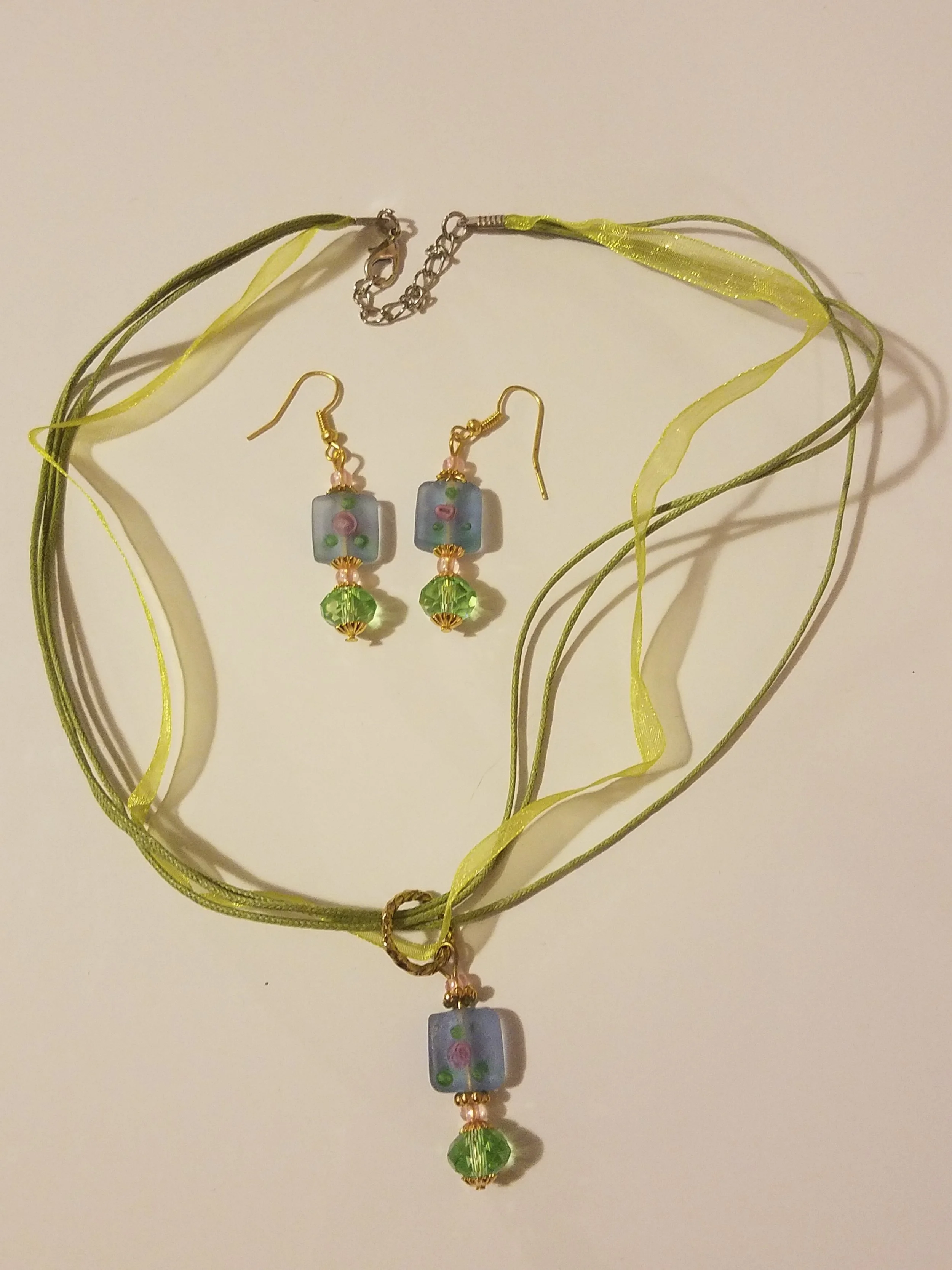 Jewelry set with a yellow ribbon necklace and matching earrings, featuring square glass beads with pink and green floral designs and green crystal beads.
