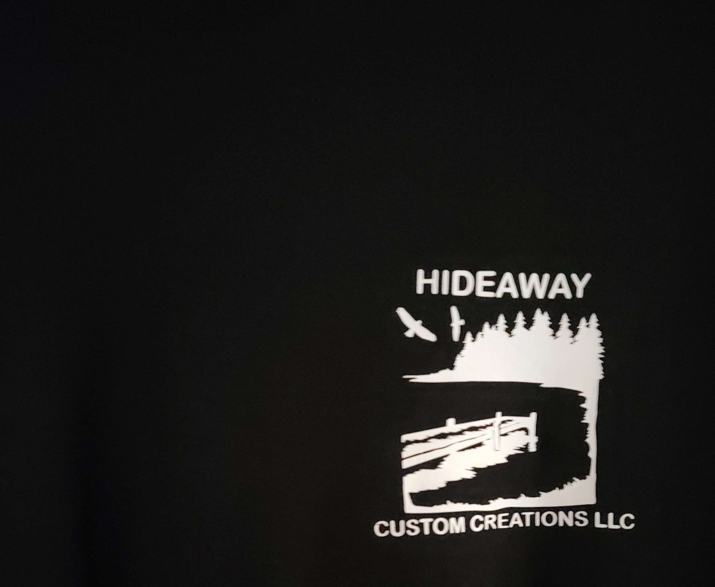 Black background with white logo and text: a pine tree, a bird flying, a hiker, and a bridge design. The text reads 'HIDEAWAY' and 'CUSTOM CREATIONS LLC'.