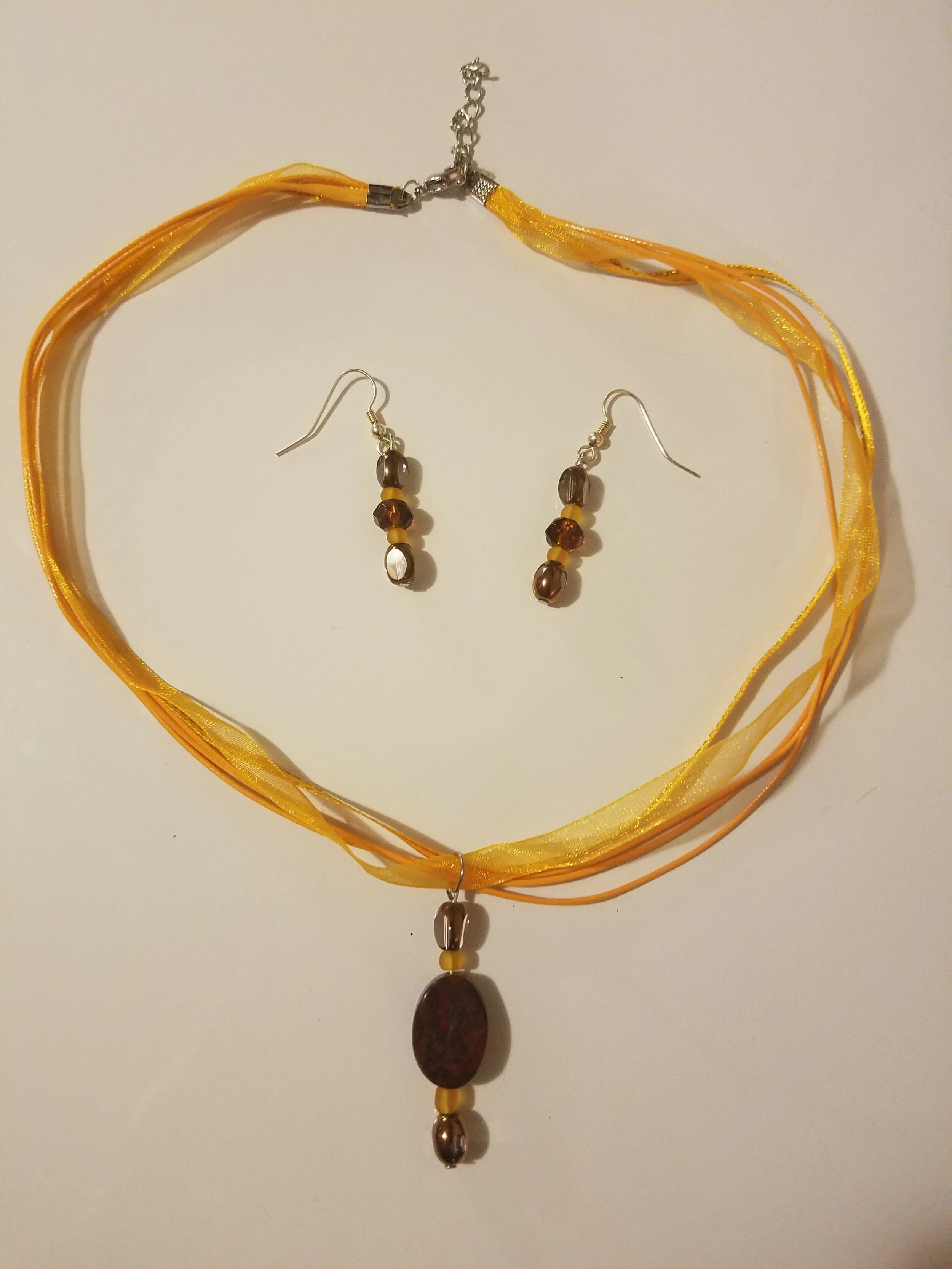 Yellow and orange ribbon necklace with a large pendant, paired with matching earrings with beads.