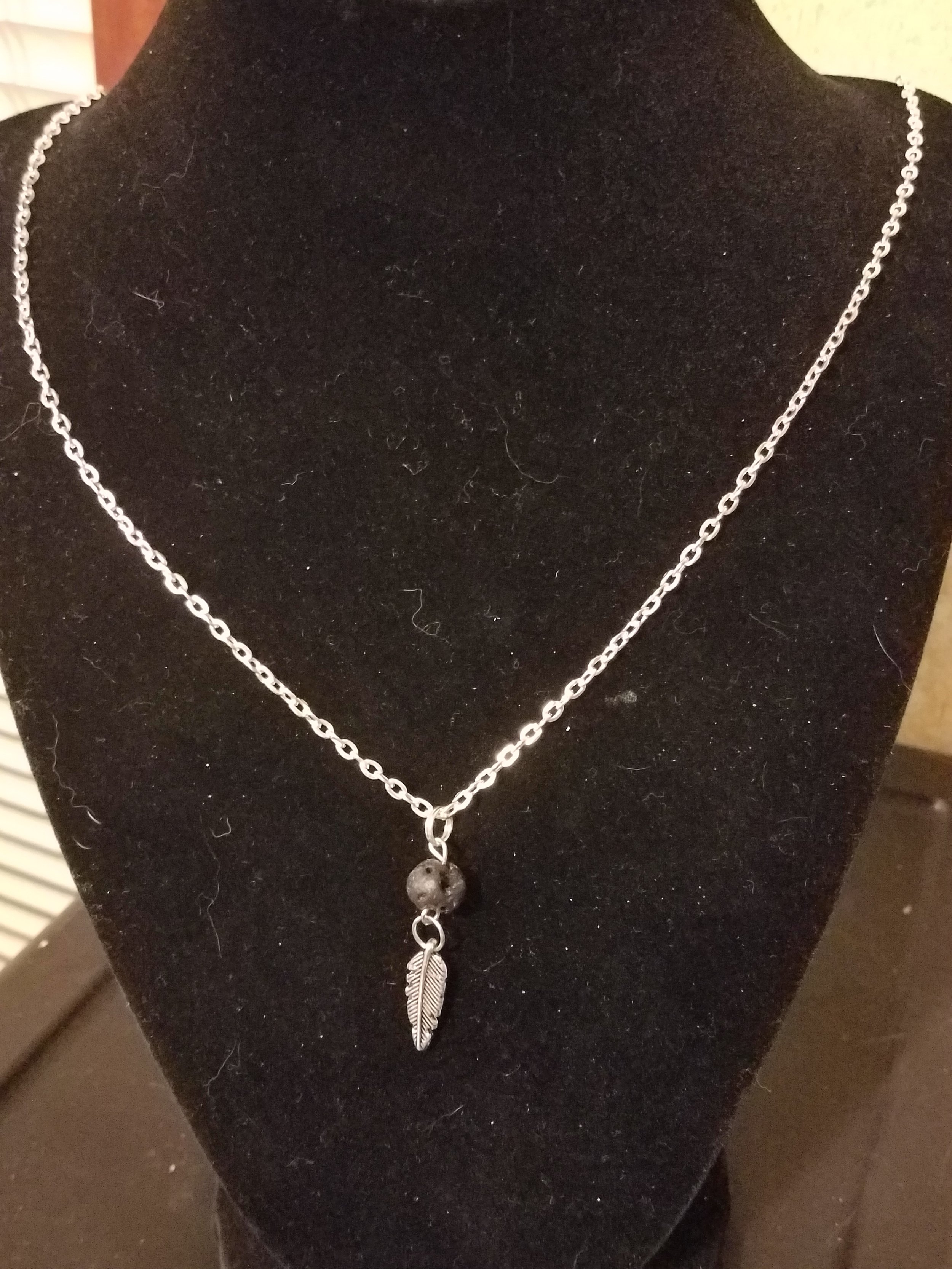 Silver necklace with a feather and bead pendant on display against a black background.