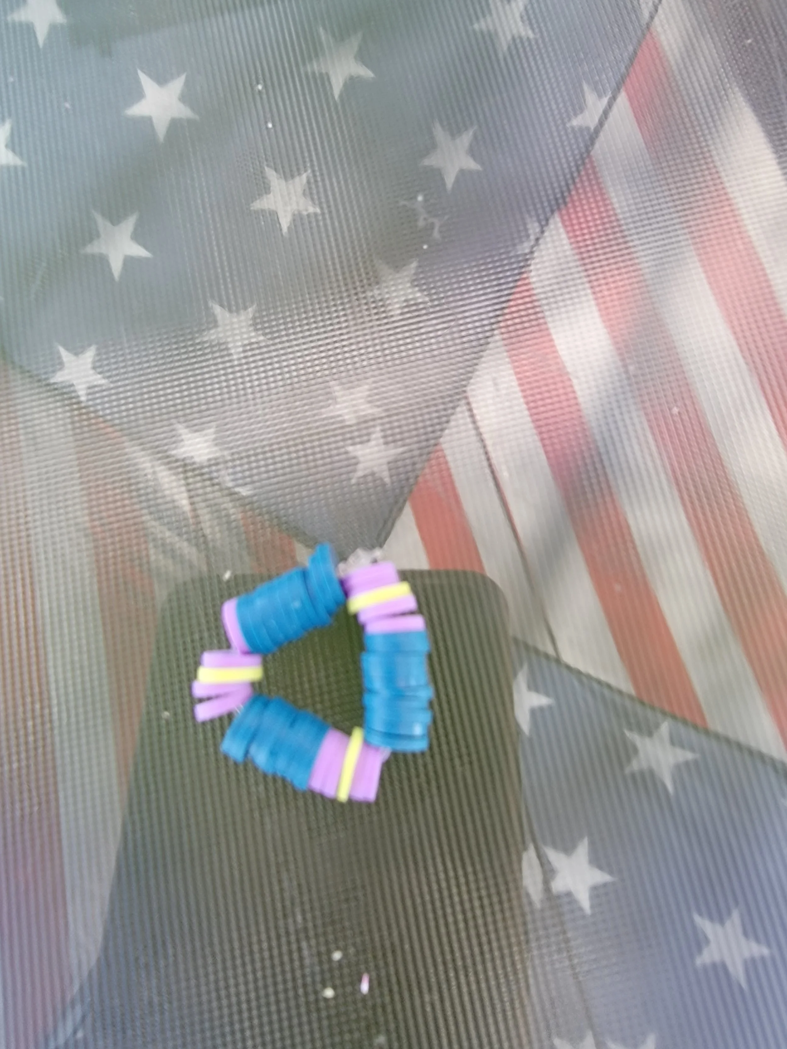 Colorful plastic bracelets arranged in a heart shape on a glass surface with an American flag pattern behind it.