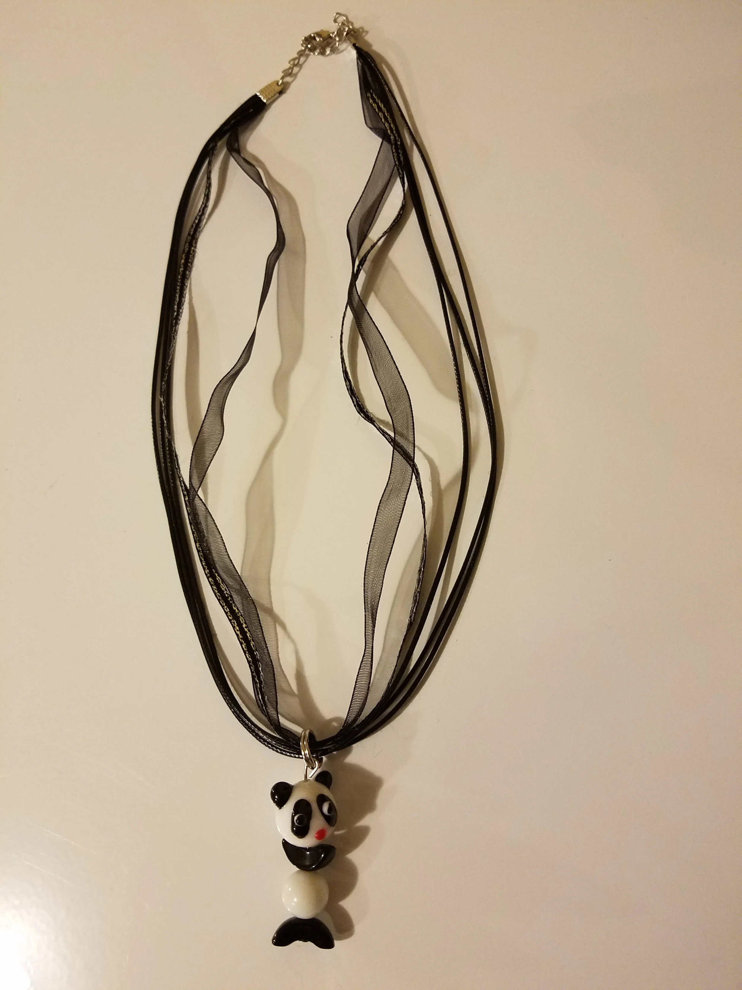 Necklace with a panda bear pendant hanging from a black ribbon.