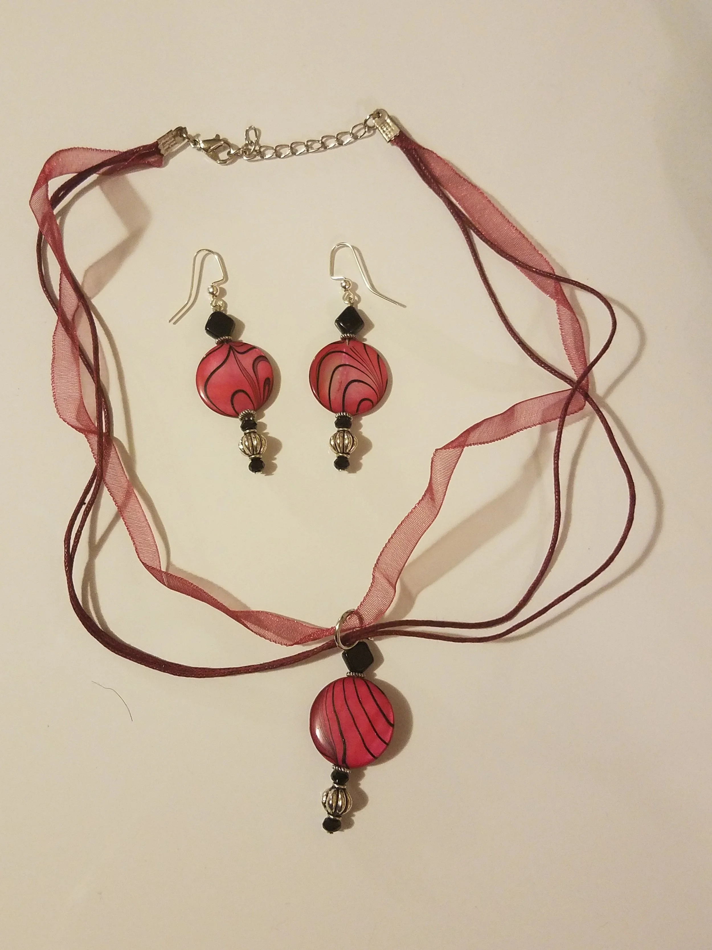 Pink and black beaded necklace with matching dangly earrings, all on a white background.