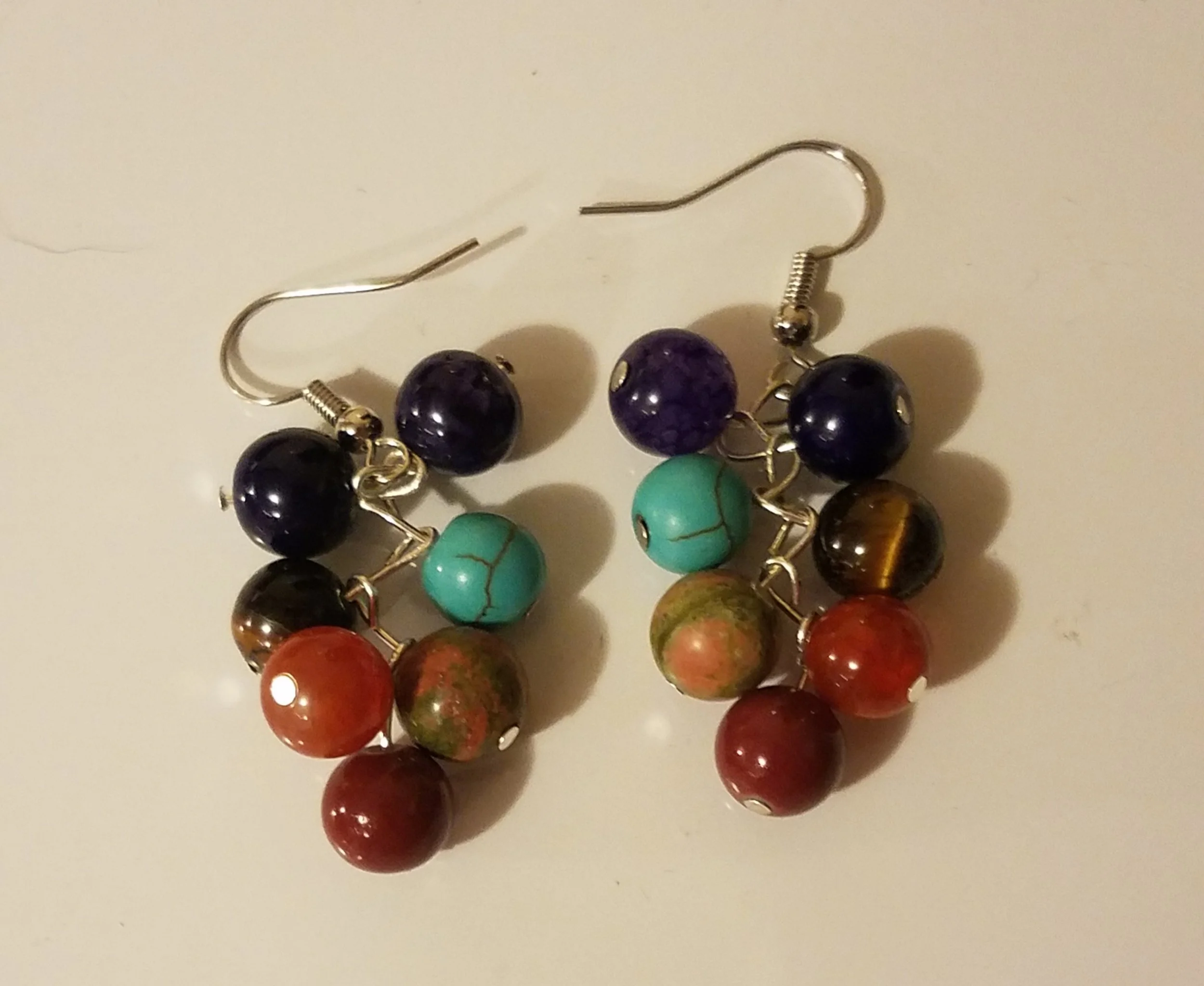 Colorful beaded earrings with round beads in purple, turquoise, tiger's eye, red, and marbled patterns, attached to silver hooks.