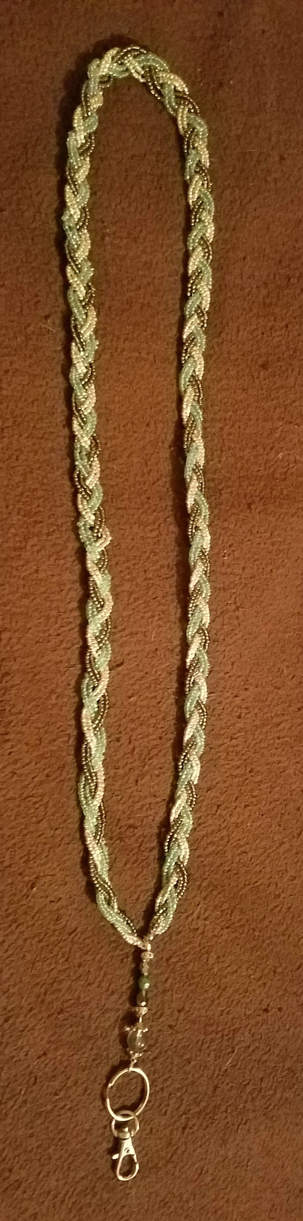Beige and gold braided beaded necklace with a clasp at the end, laying on a brown surface.