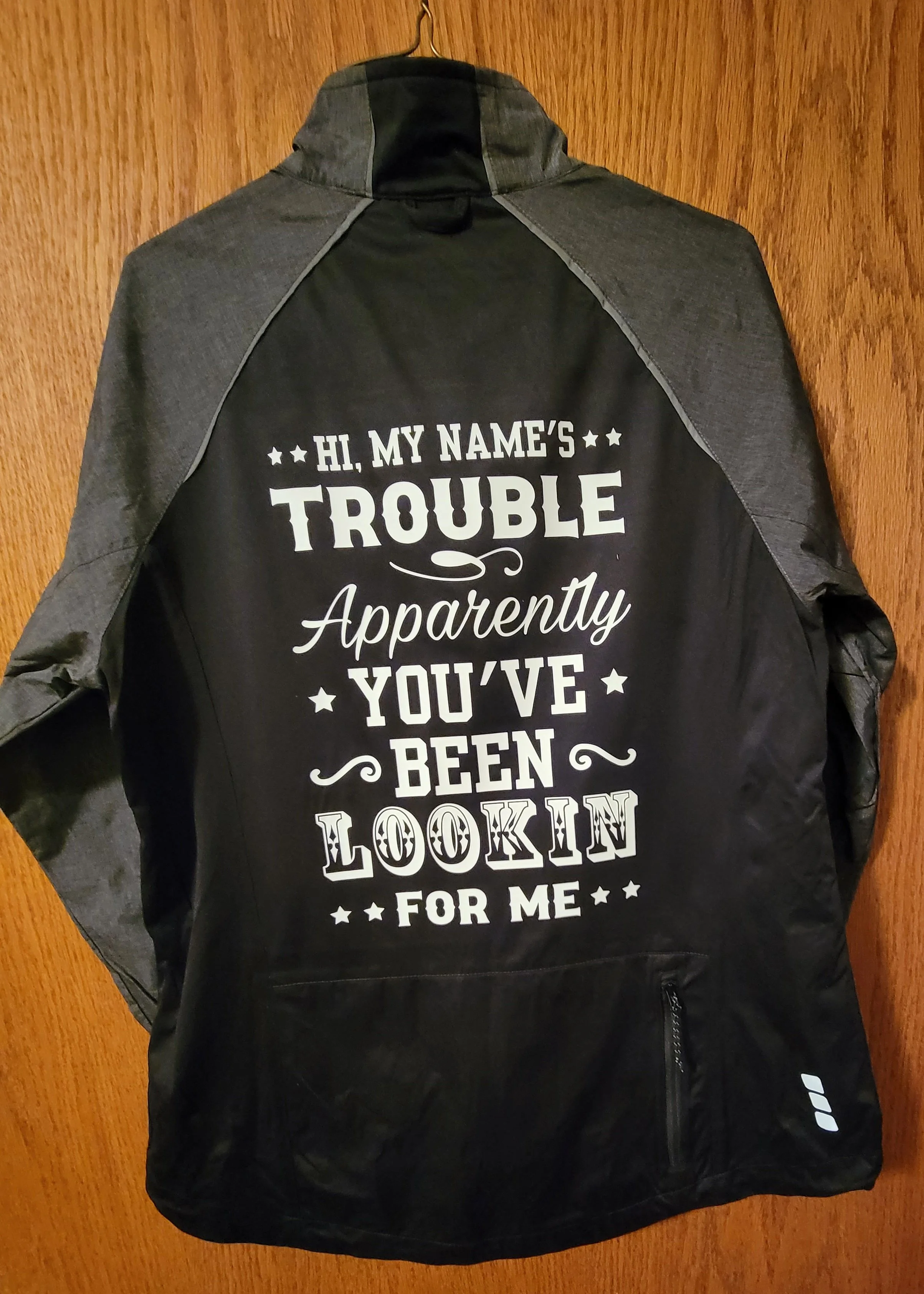 black and gray outdoor jacket with a humorous phrase printed on the back in white text, referencing being looked at by others.