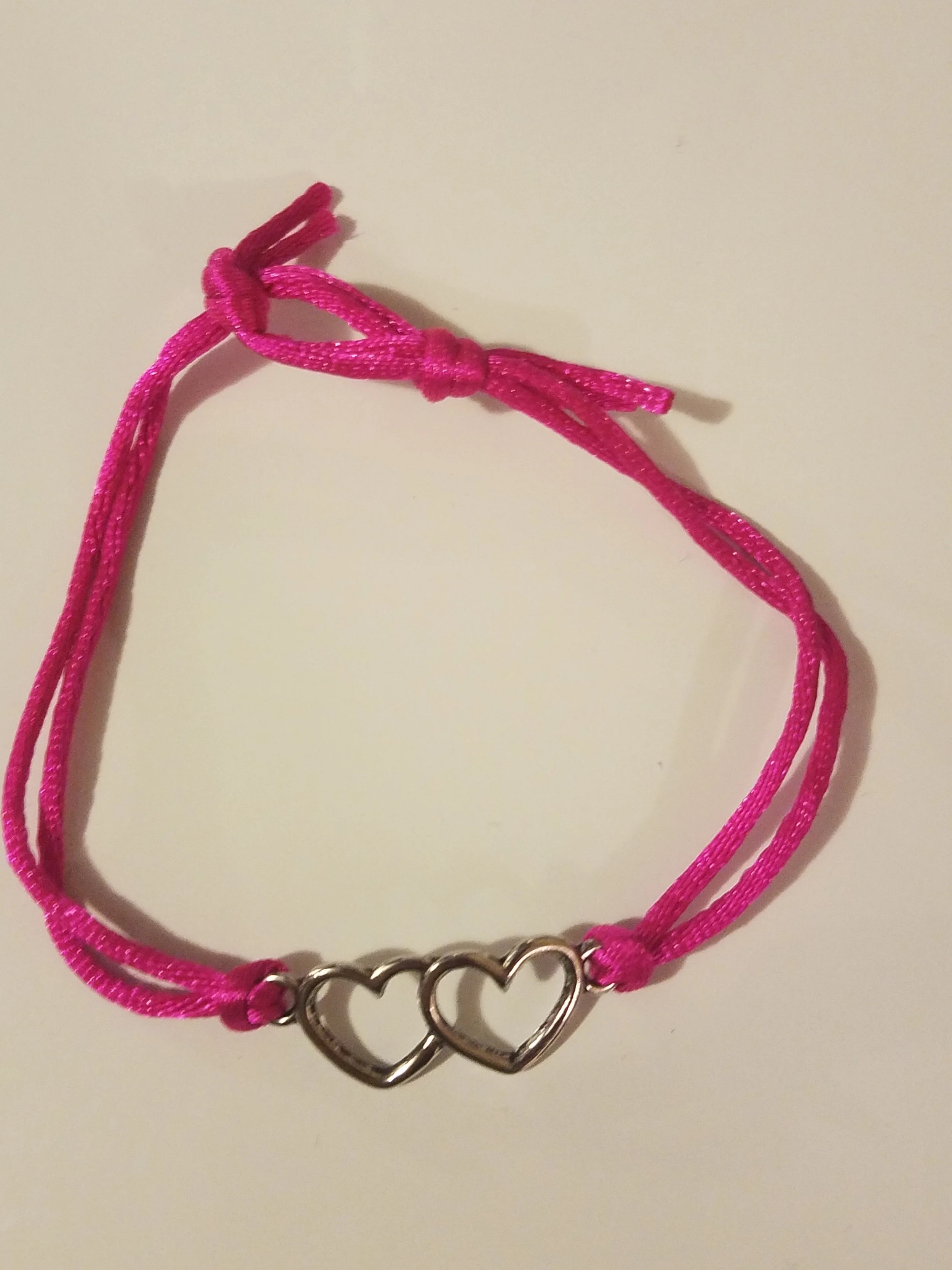 Pink cord bracelet with two interlocking heart charms.