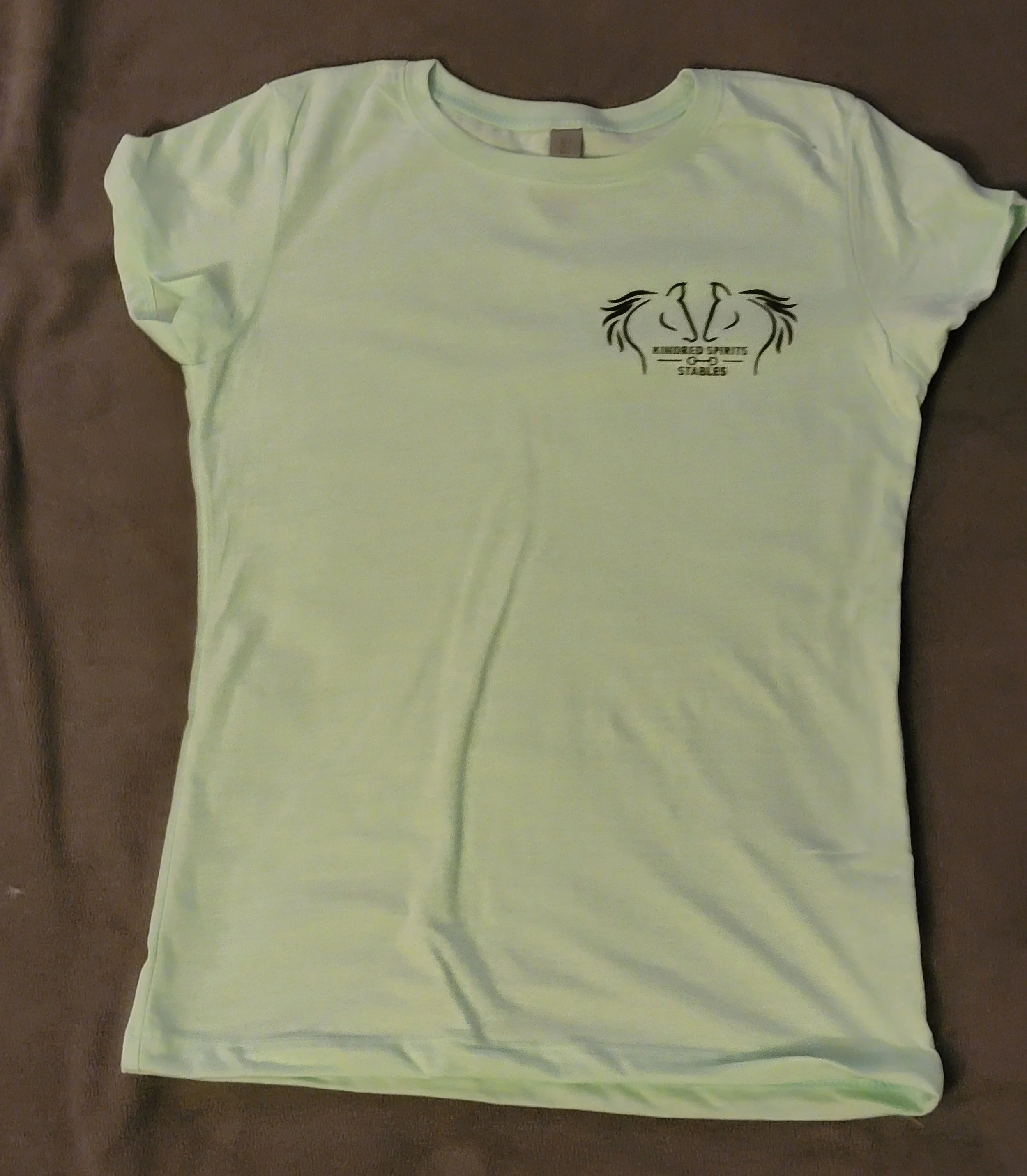 Light yellow T-shirt lying flat with a small logo of two horse heads facing each other and the text 'VINDOR SPORTS GREATS' on the upper left chest area.