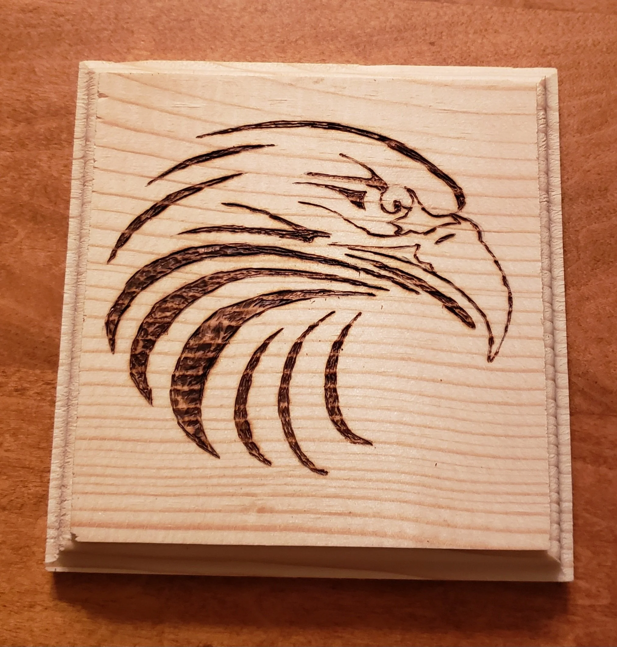 Wooden block with a black line drawing of a bird's head and feathers.