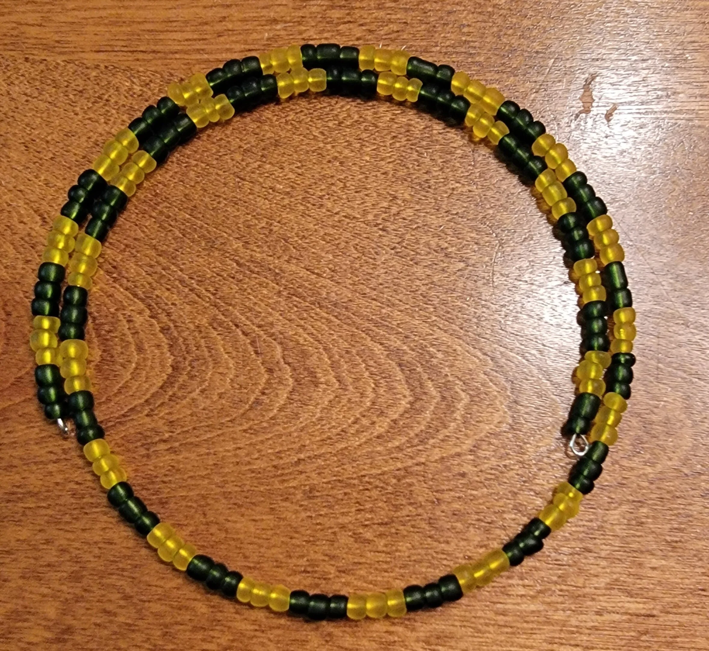 A beaded necklace made of small black and yellow beads arranged in a pattern, resting on a wooden surface.