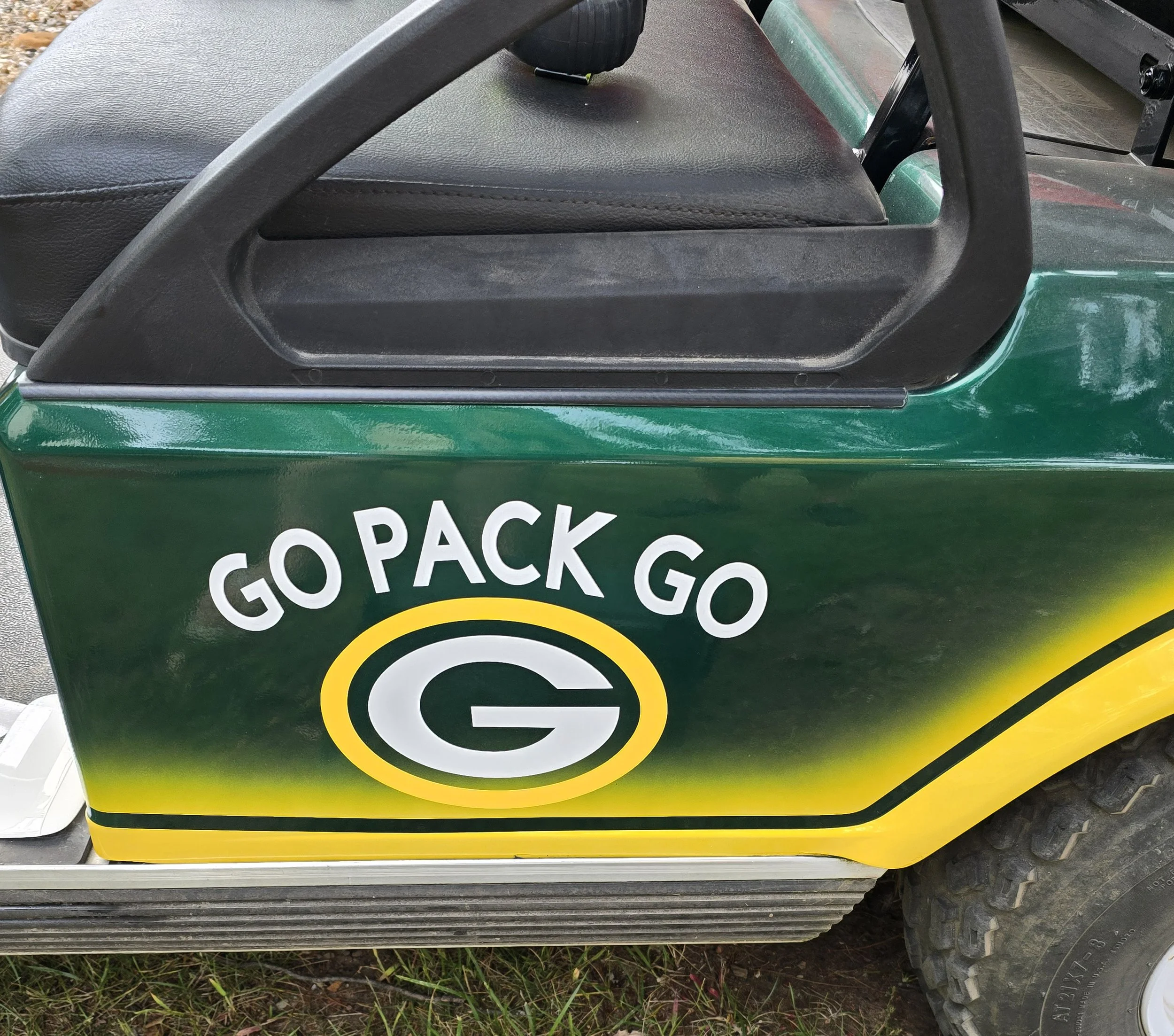 A golf cart with a Green Bay Packers theme, featuring the phrase 'GO PACK GO' and the Packers logo on its side.