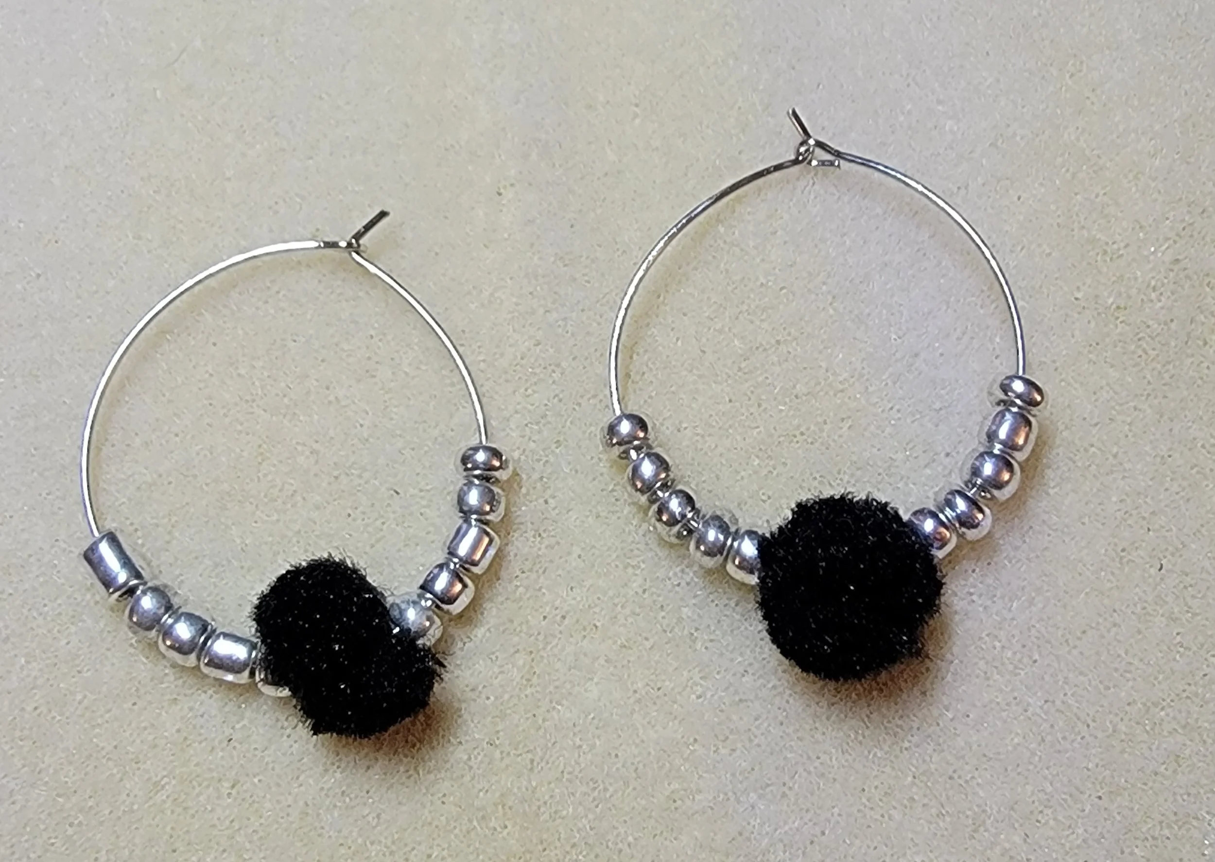 Silver hoop earrings with small silver beads and black pom-pom on each.