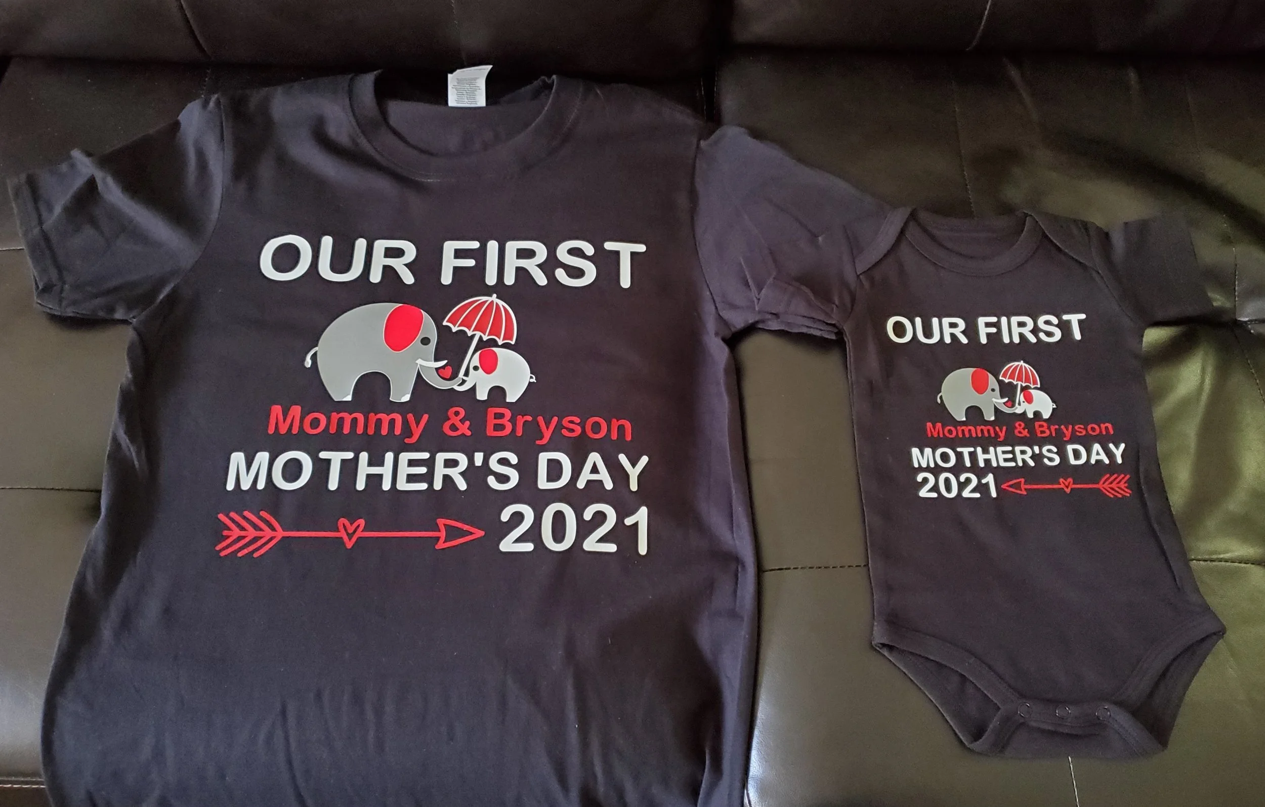 Matching black t-shirts for Mother's Day 2021 featuring cartoon elephants, one larger and one smaller, with a red umbrella, the text "Our First Mommy & Bryson MOTHER'S DAY 2021" and a red arrow design.