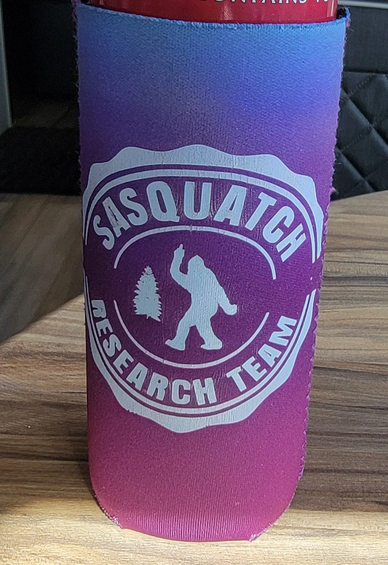 A tumbler with a Sasquatch Research Team logo, featuring a silhouette of Bigfoot, a tree, and text in purple, pink, and white colors.