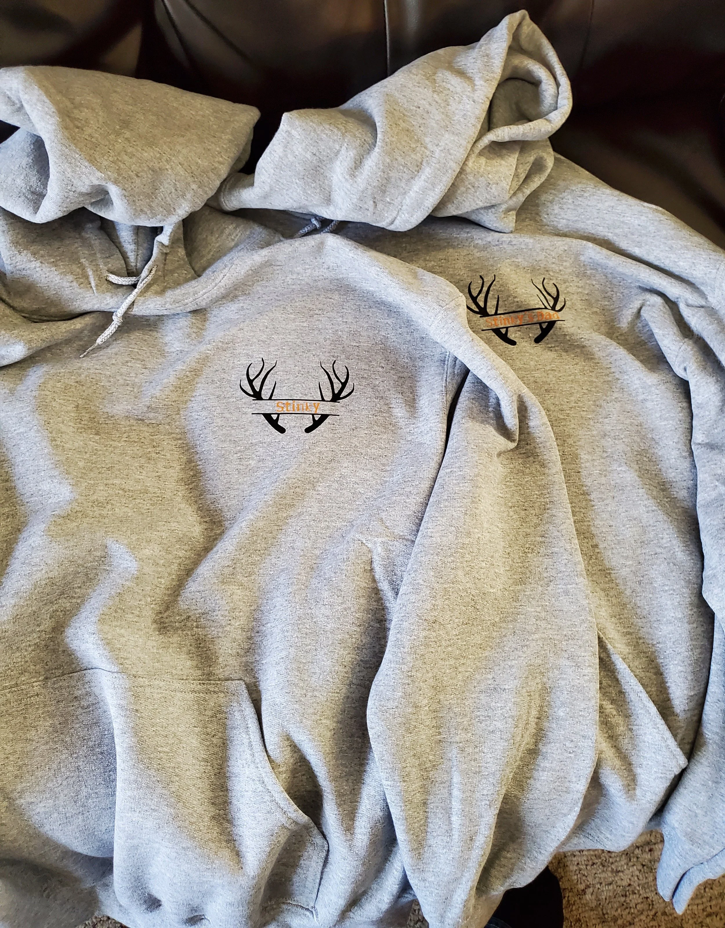 A gray hoodie with a black and orange logo featuring antlers and the word 'Stinky.' placed on the chest area.