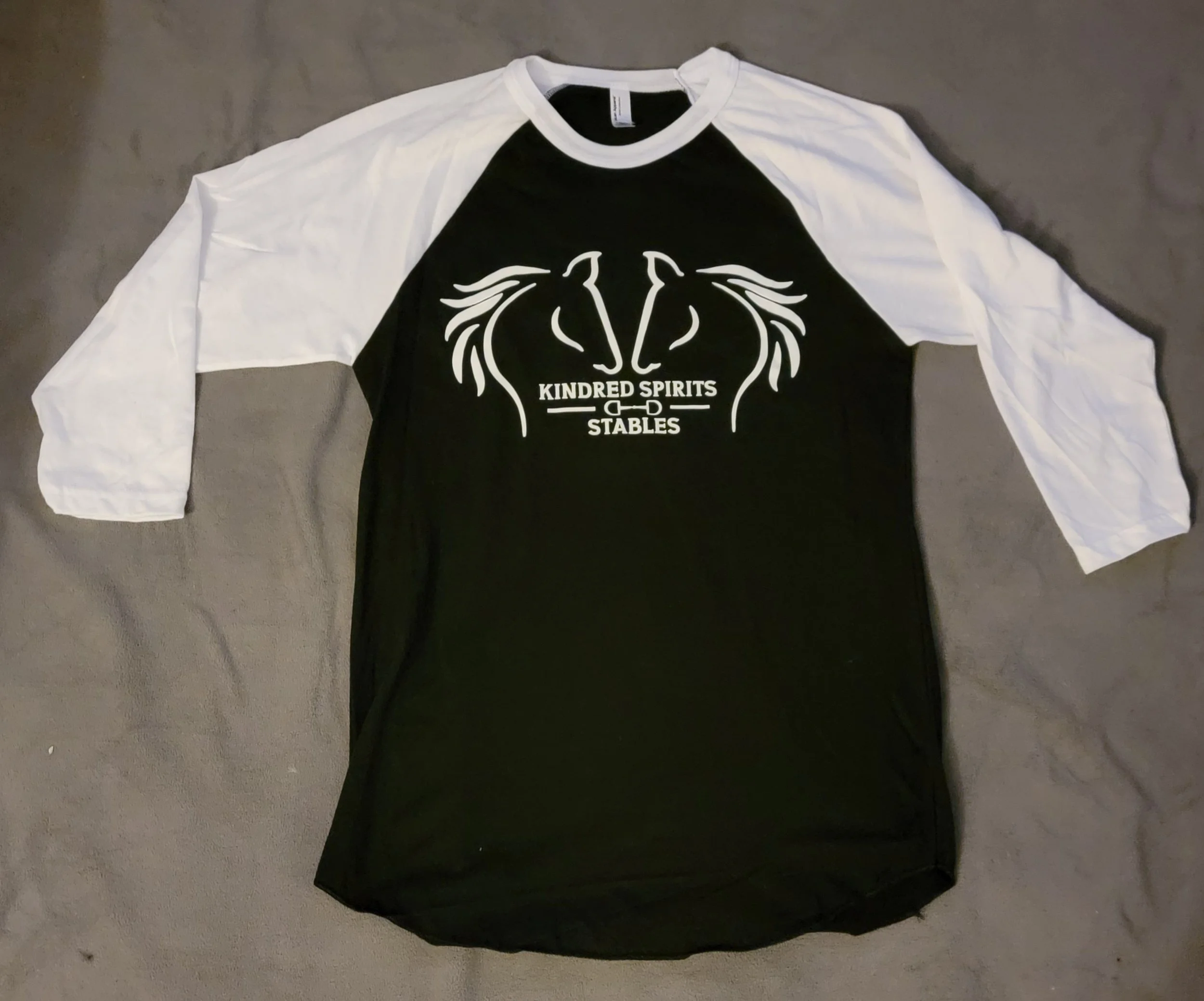 Black and white baseball-style t-shirt with the logo 'KINDRED SPIRITS STABLES' and an illustration of two horse heads facing each other.