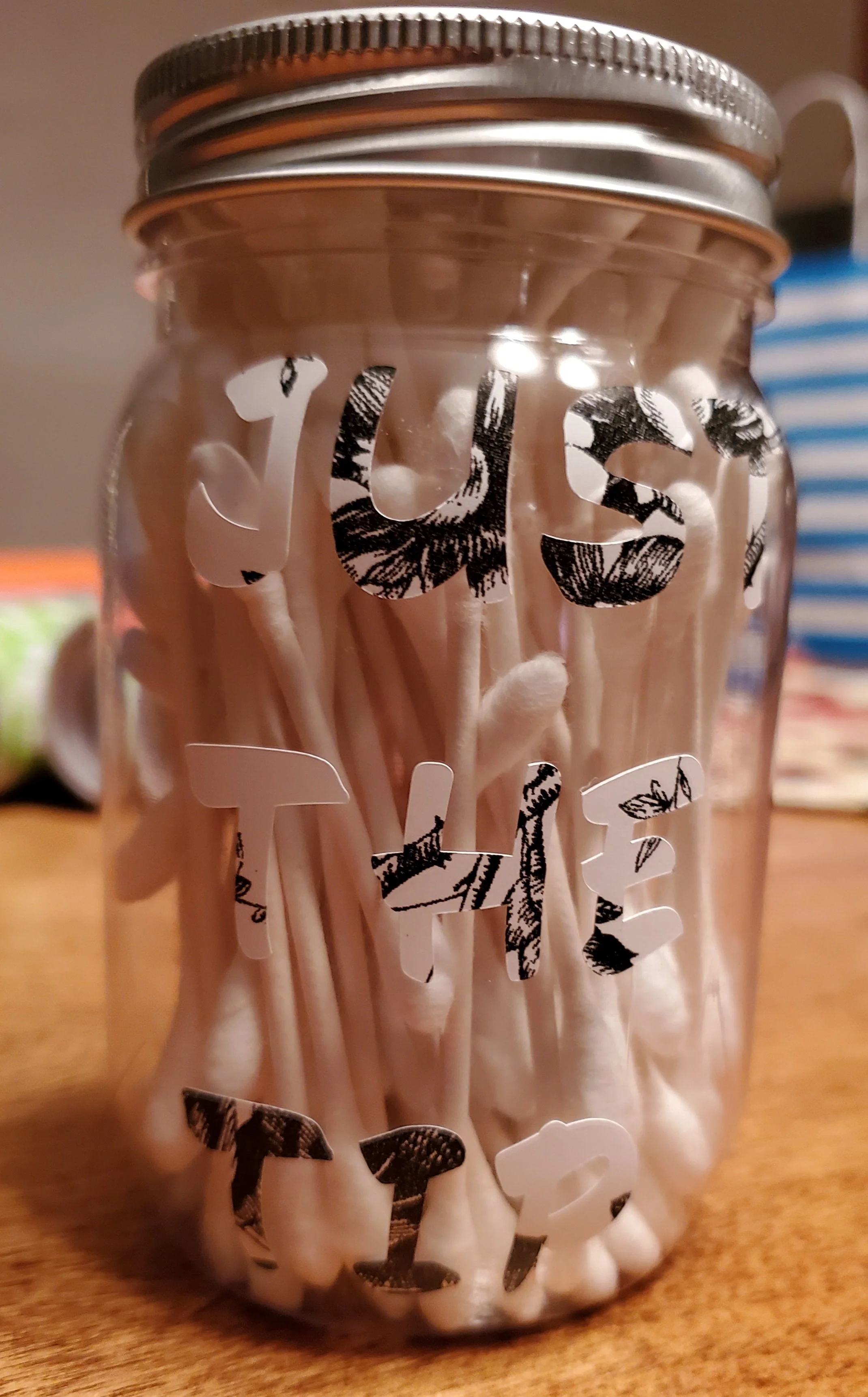 A glass jar with the words 'LOVE THIS' written with black and white patterned letters, filled with white cotton swabs.