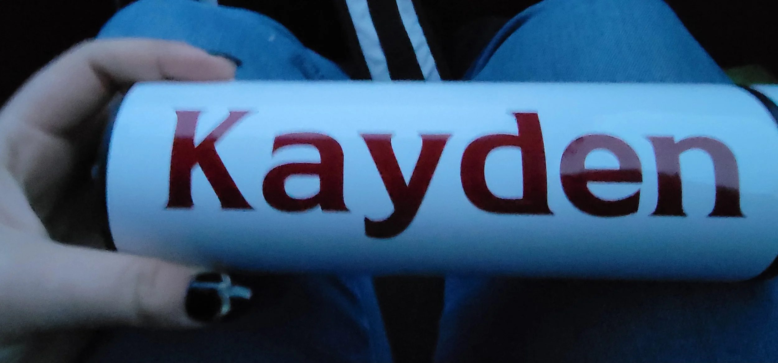Close-up of a hand holding a cylindrical object with the word 'Kayden' in large red and black letters on a white background.