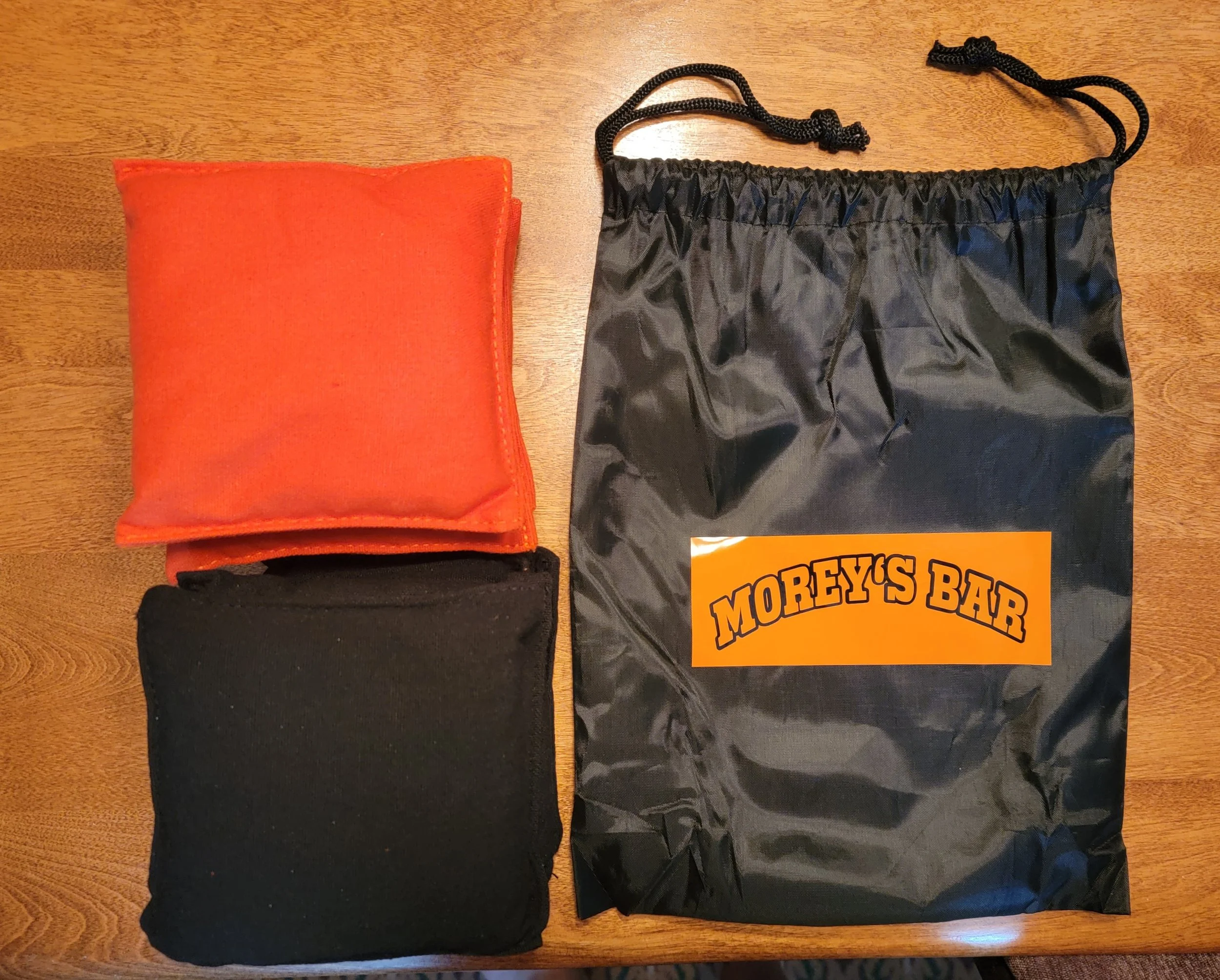 A black drawstring bag labeled "Morey's Bar," two folded pieces of clothing in orange and black, placed on a wooden surface.