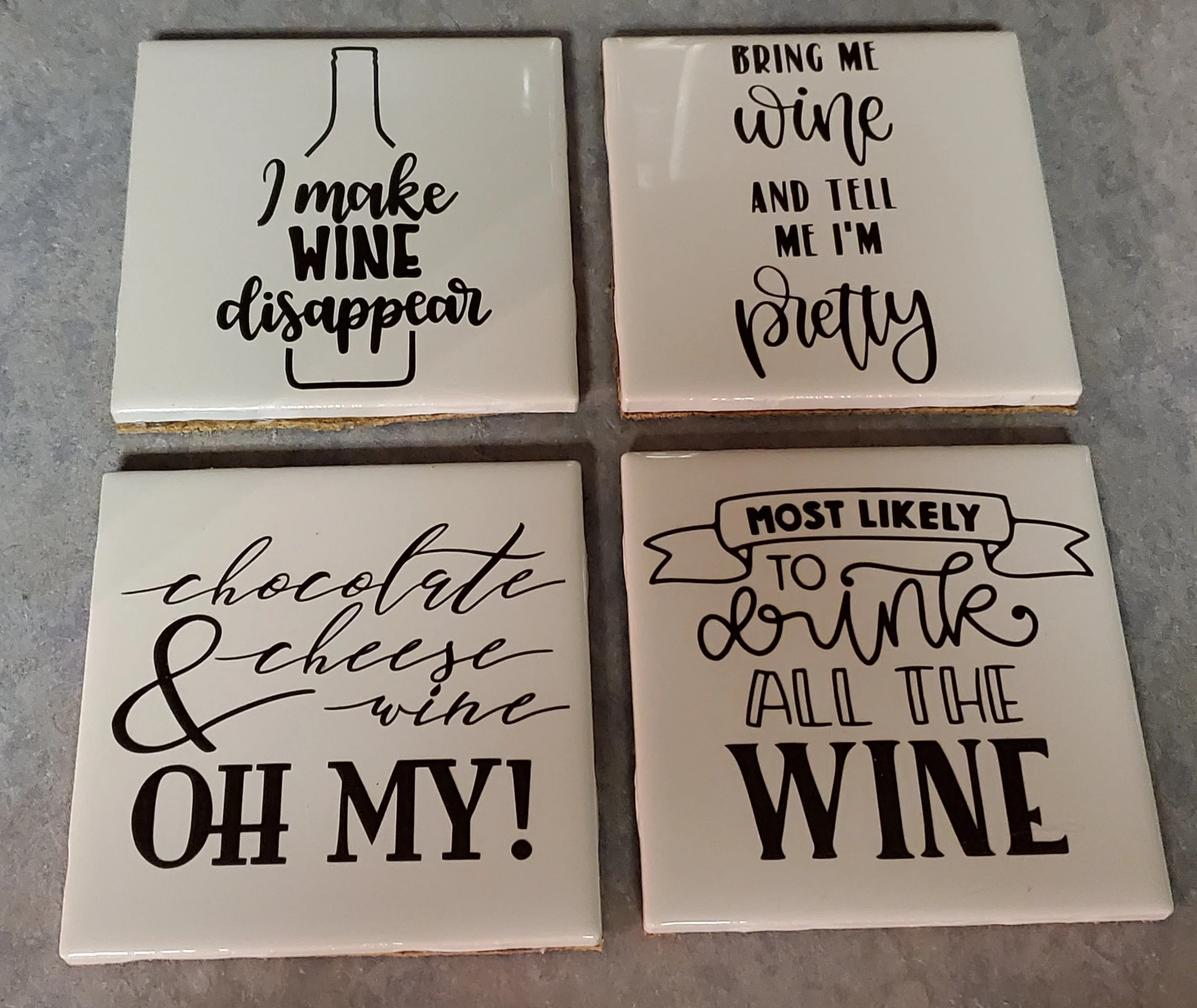 Four decorative tiles with wine-themed quotes in black text on a white background. Top left tile: 'I make wine disappear' with a wine bottle outline. Top right tile: 'Bring me wine and tell me I'm pretty.' Bottom left tile: 'Chocolate, cheese, wine, 