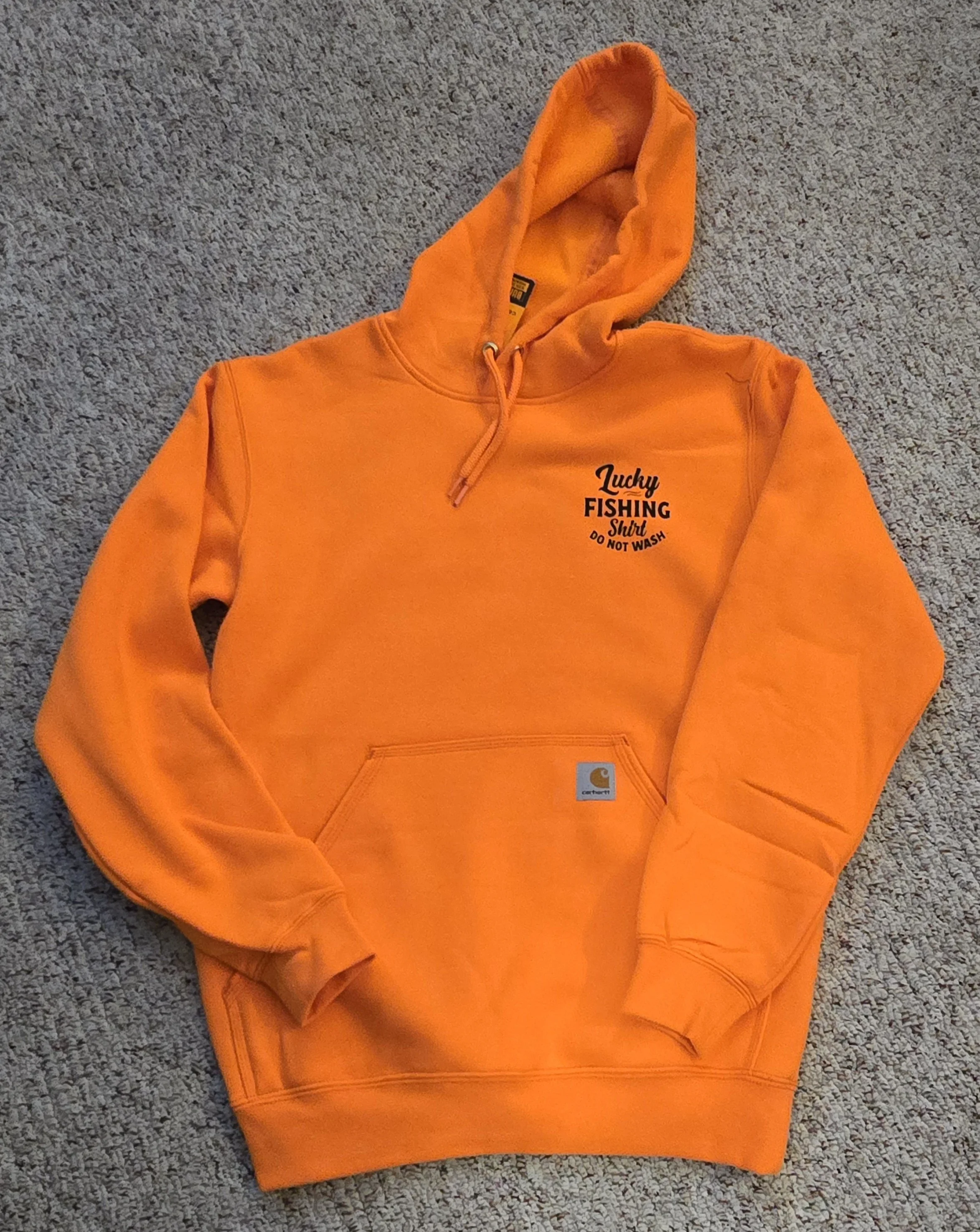 Orange Carhartt hoodie with front pocket and drawstring hood, featuring text that says 'Lucky Fishing Shirt, Do Not Wash'.