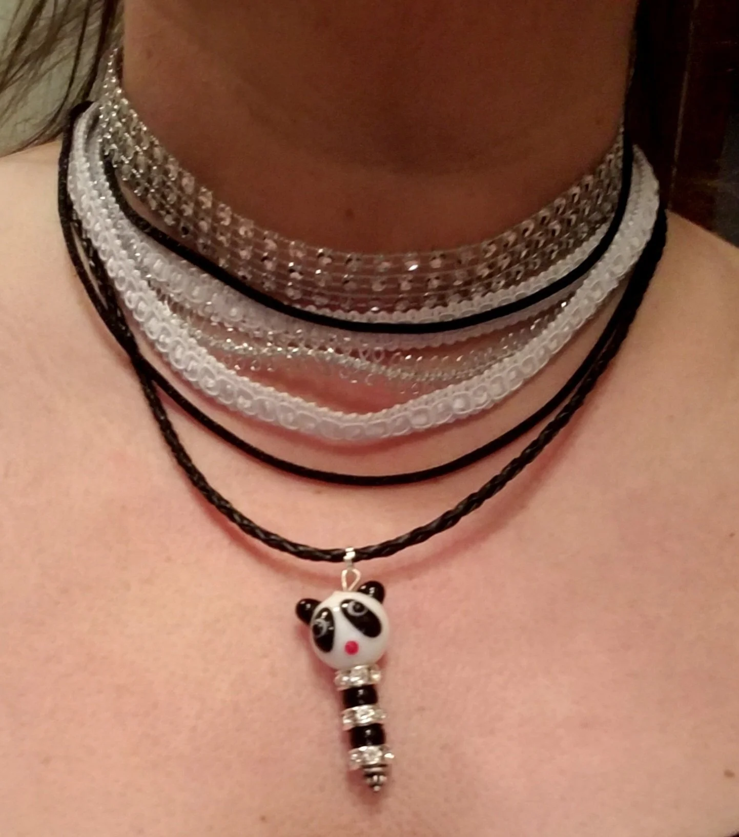 Close-up of a person's neck and chest wearing layered necklaces, including a panda pendant necklace, with various chains and beads.