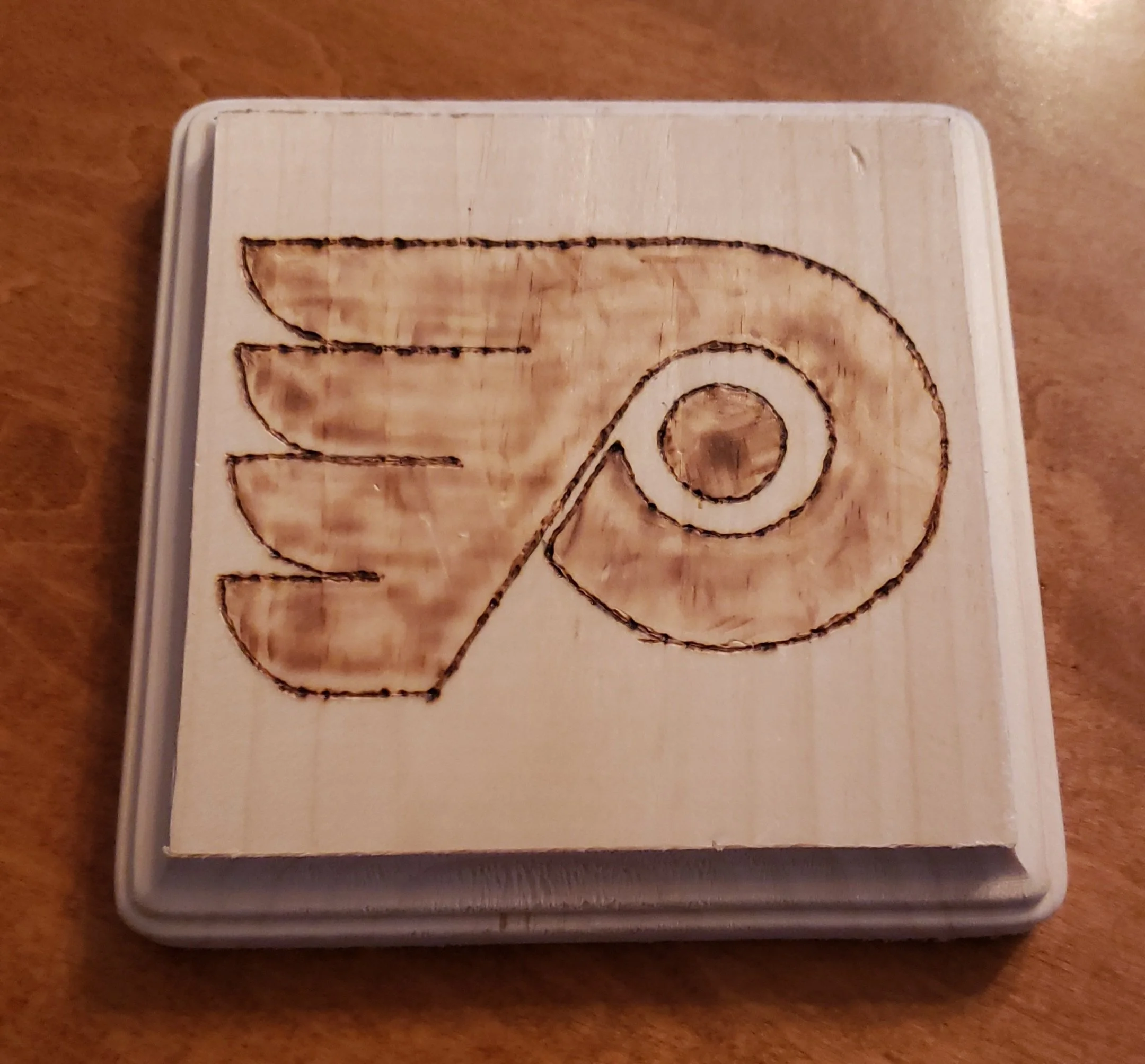 A wooden square with the Starbucks logo burned and etched onto the surface.