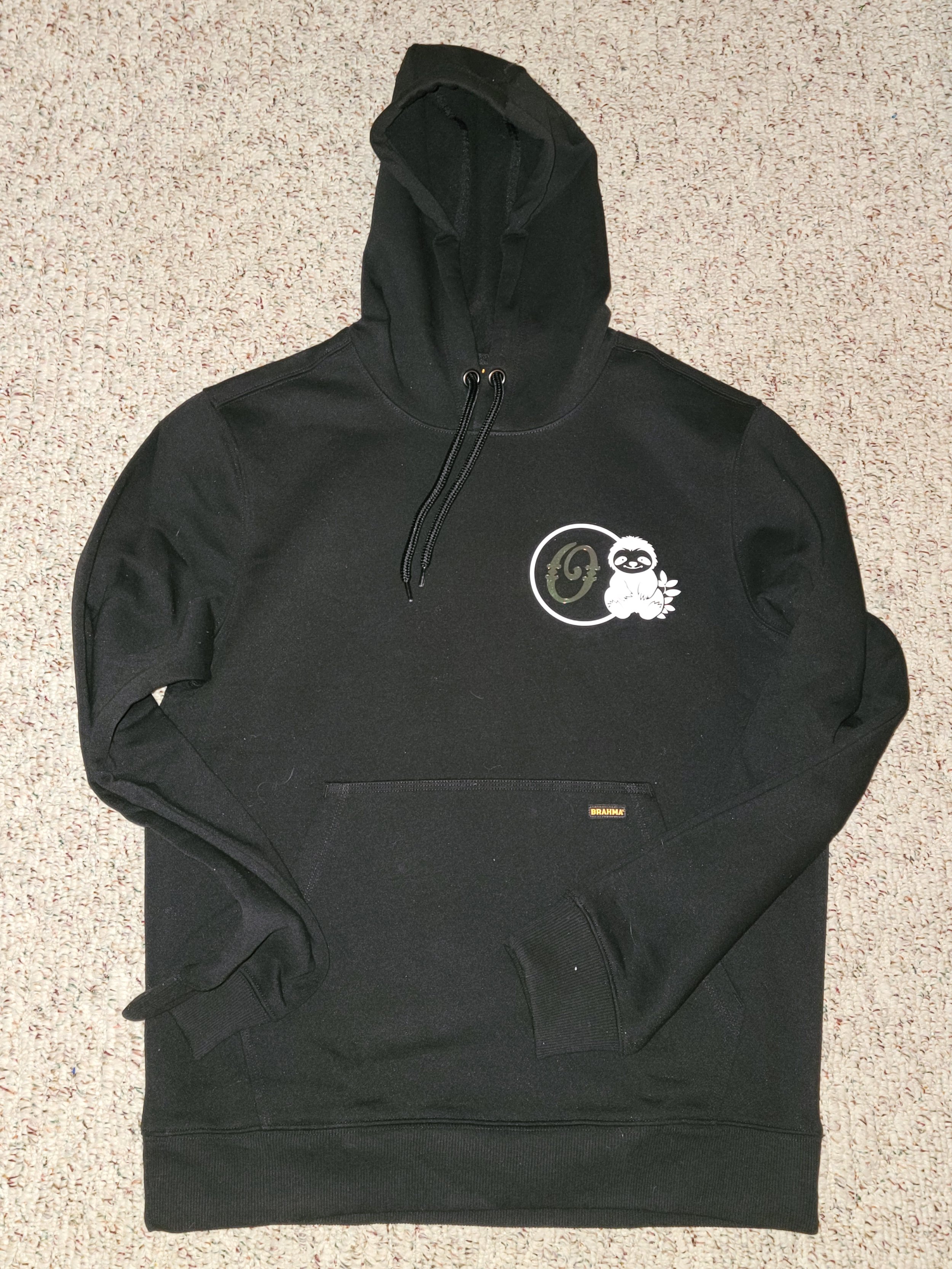 Black hooded sweatshirt with a logo featuring a sloth holding a leaf and a stylized Earth, laid flat on a carpet.