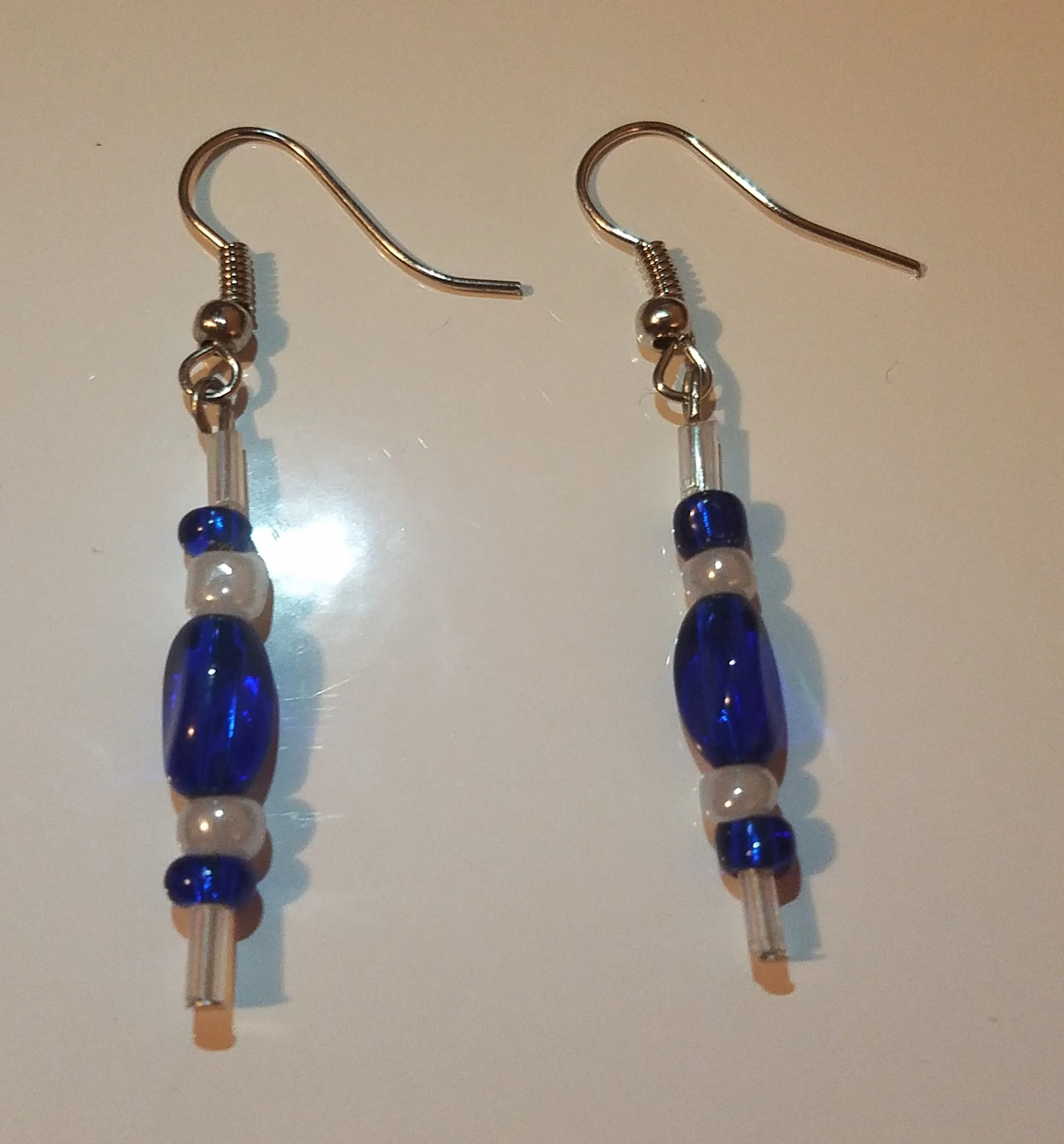Pair of dangling earrings with blue and white beads on metal hooks.