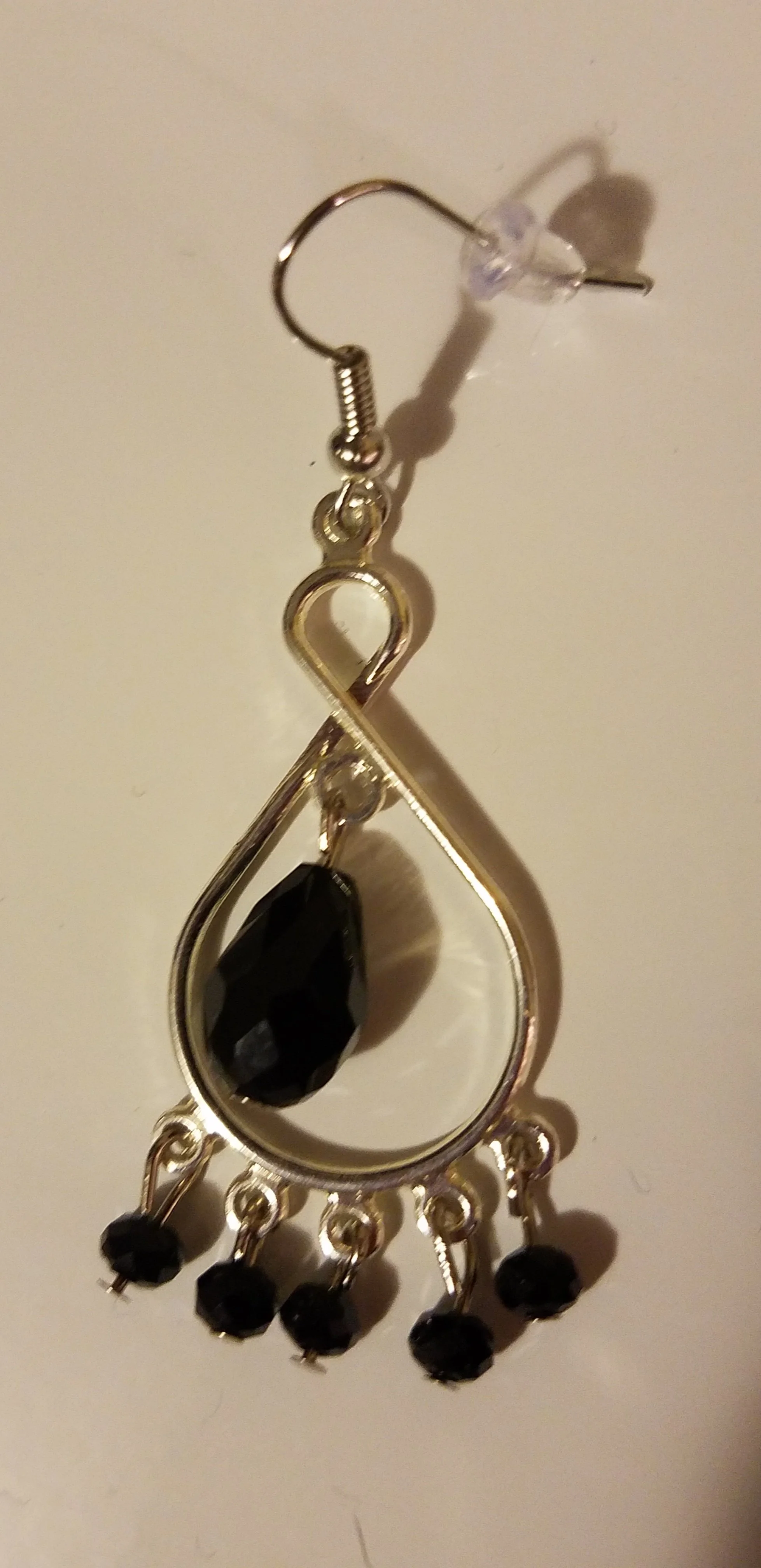 A dangling earring with a silver setting, black faceted stone, and small black beads hanging from the bottom.