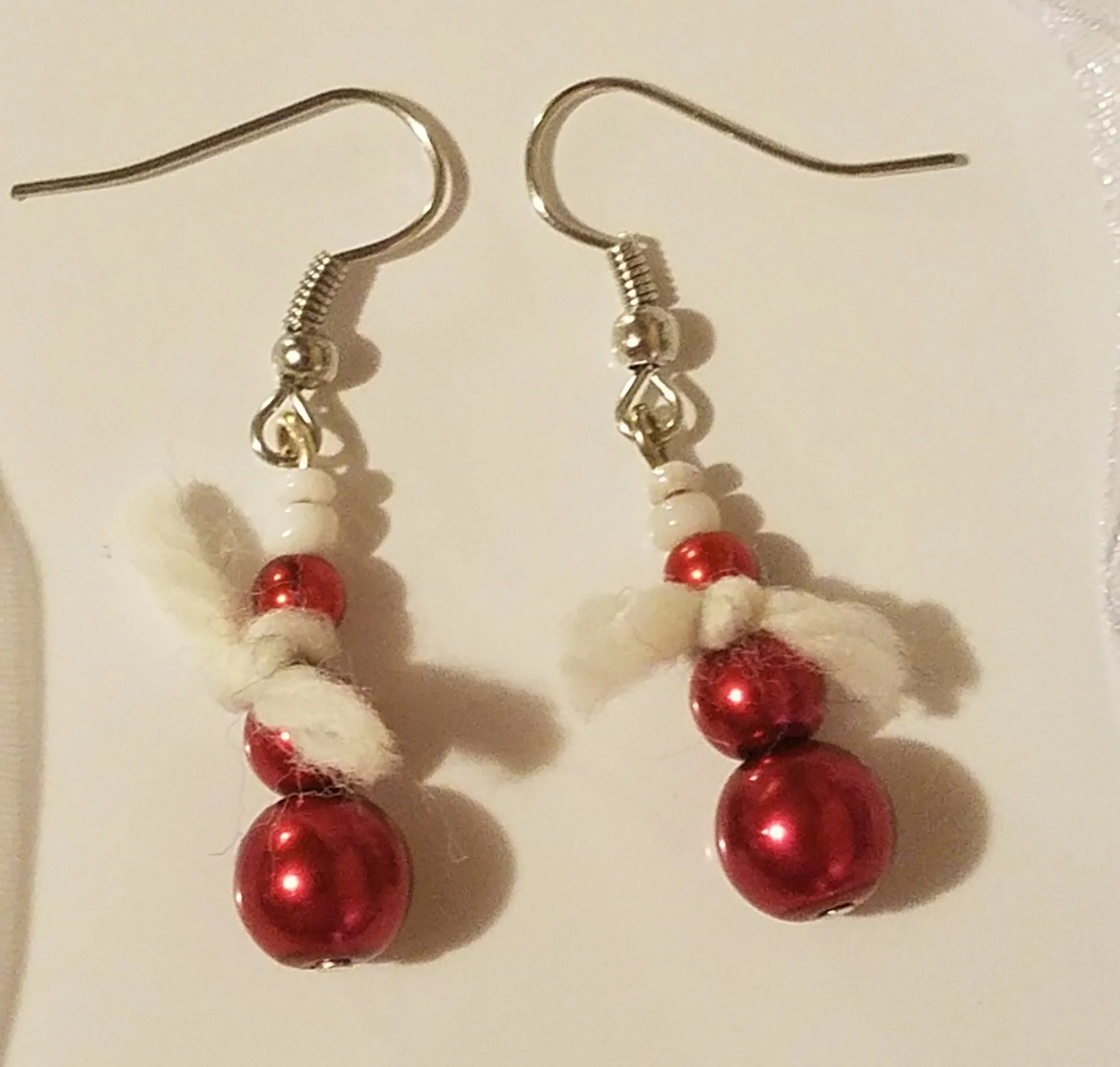 Christmas-themed earrings with red and white beads, featuring cotton-like material, hanging from silver hooks.