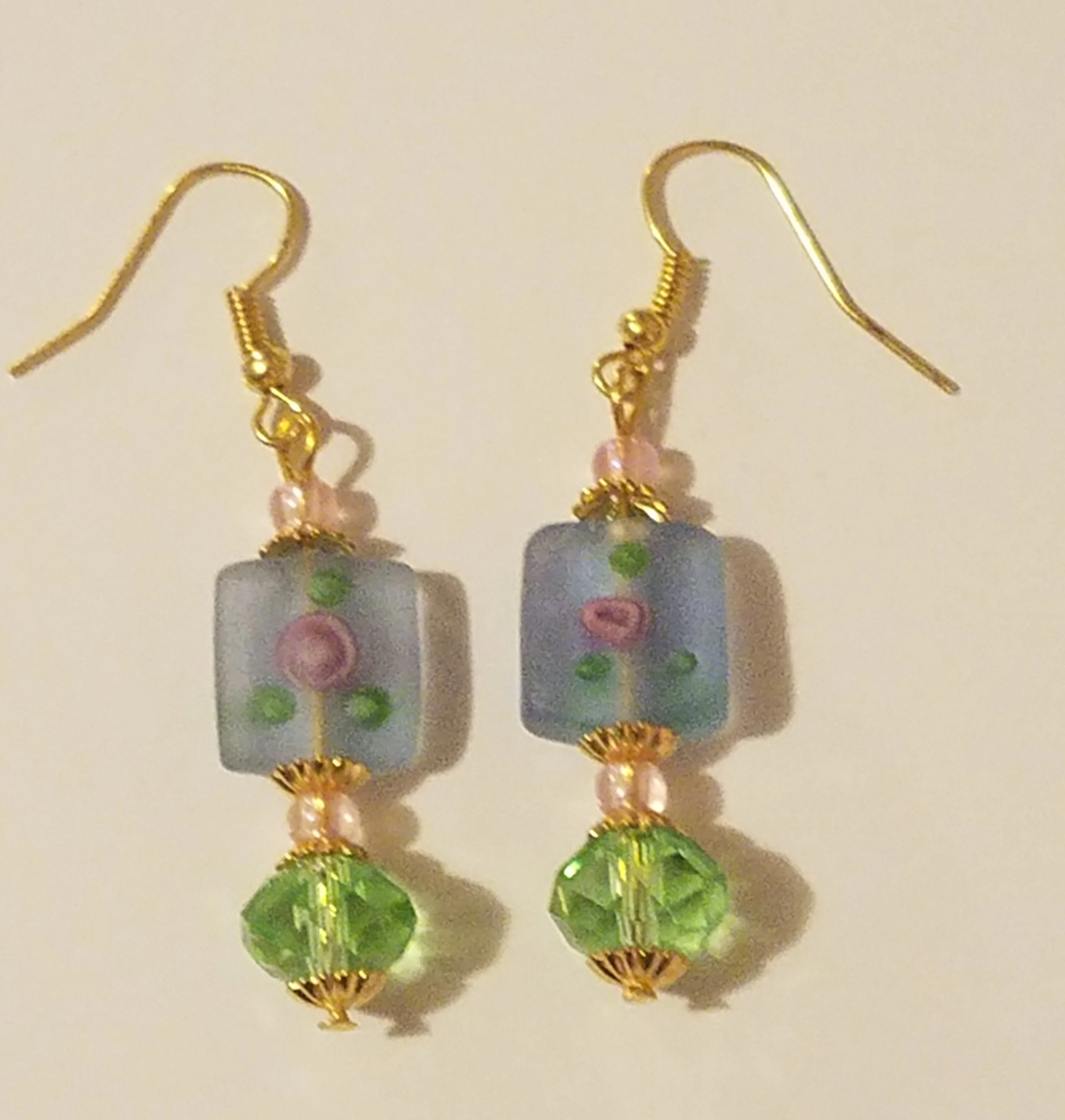 Pair of earrings with rectangular pastel beads, pink and green accents, and green faceted crystal dangles, with gold hooks.