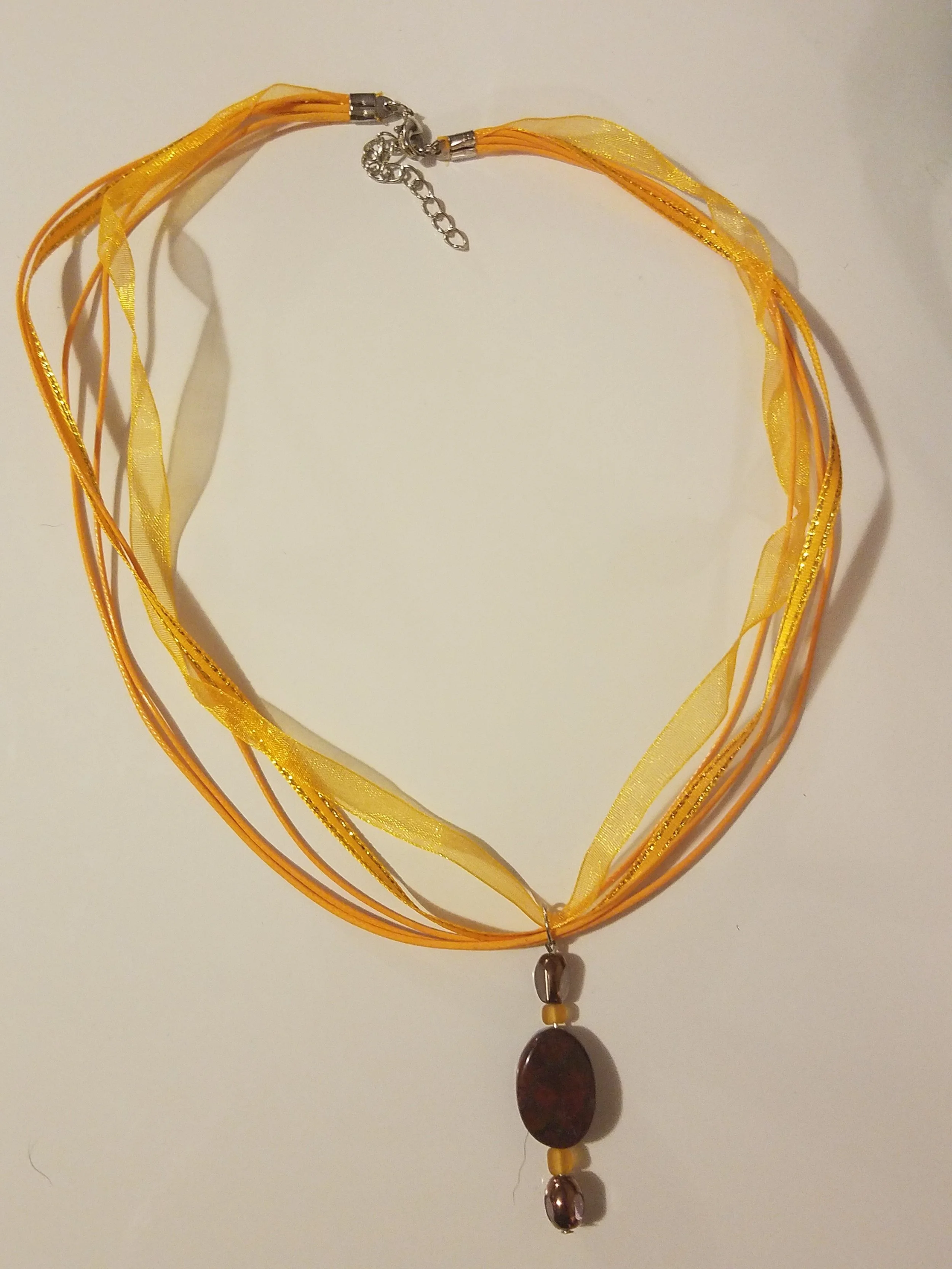 Multi-strand yellow and orange ribbon necklace with a hanging oval stone pendant and small round beads, finished with a metal clasp.