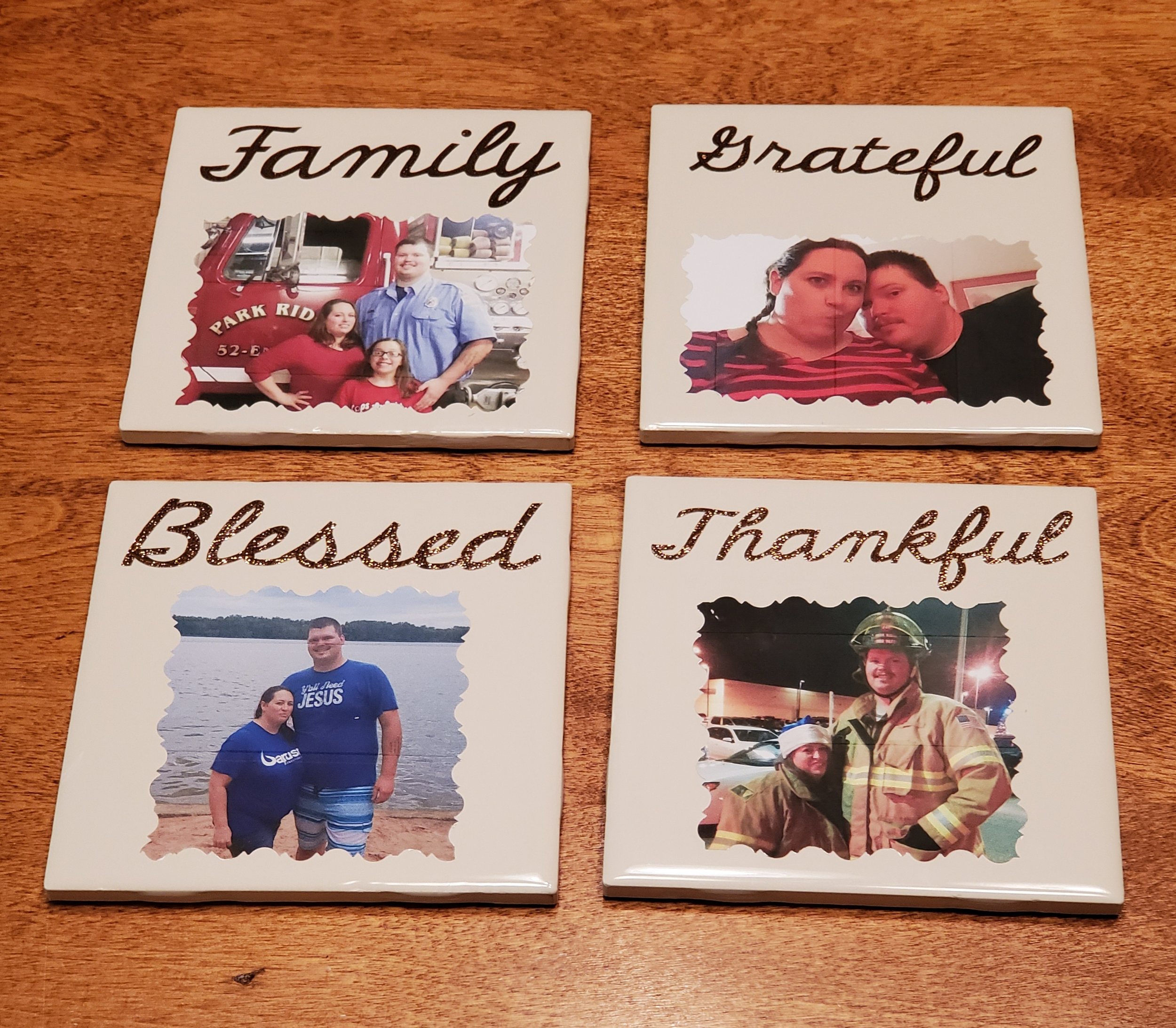 Four decorative tiles with family-themed words and photos on a wooden surface. Top left tile says 'Family' with a photo of a family in front of a fire truck. Top right tile says 'Grateful' with a photo of a woman and a man. Bottom left tile says 'Ble