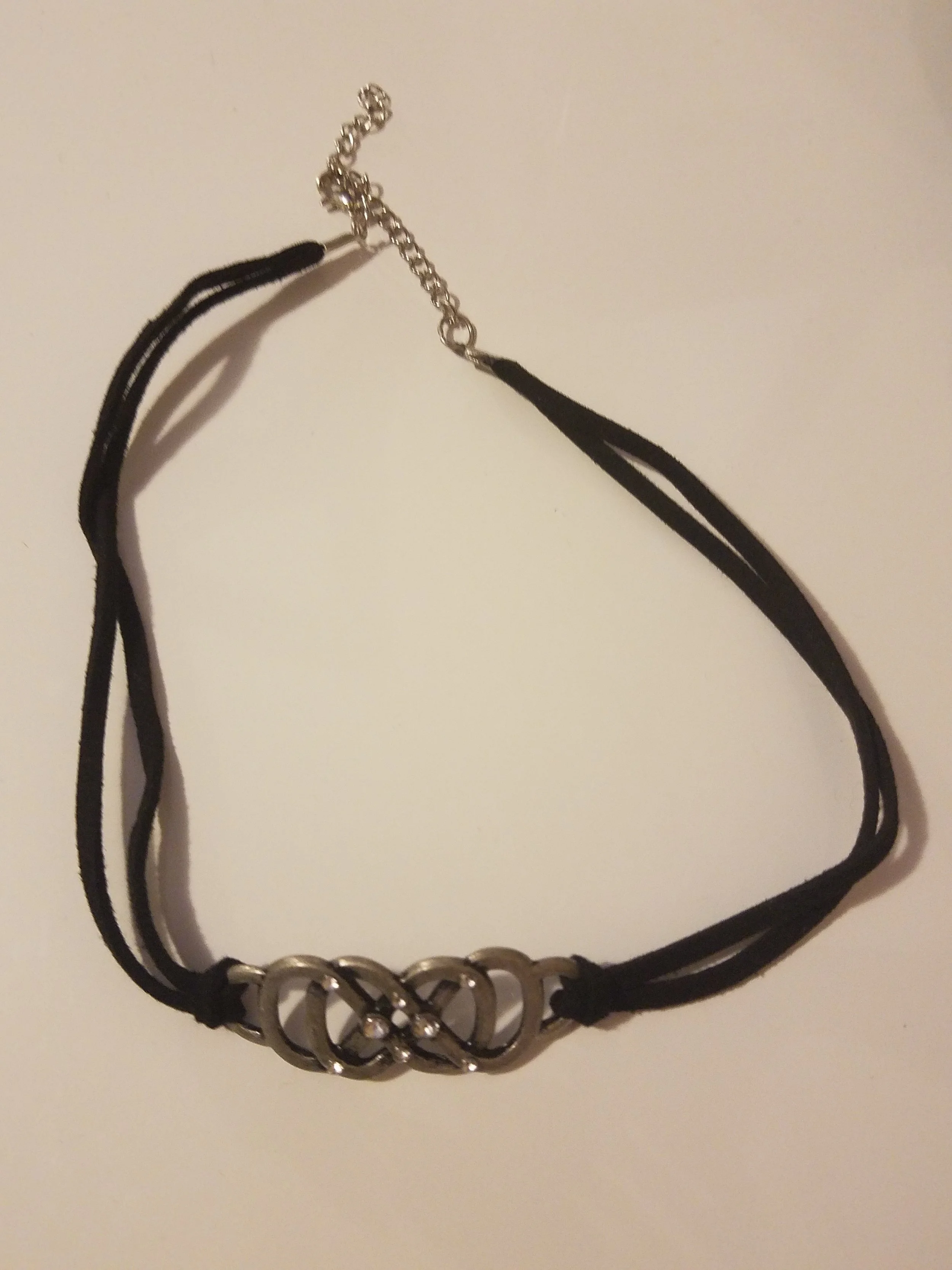 Black choker necklace with a silver heart-shaped clasp on a white surface.