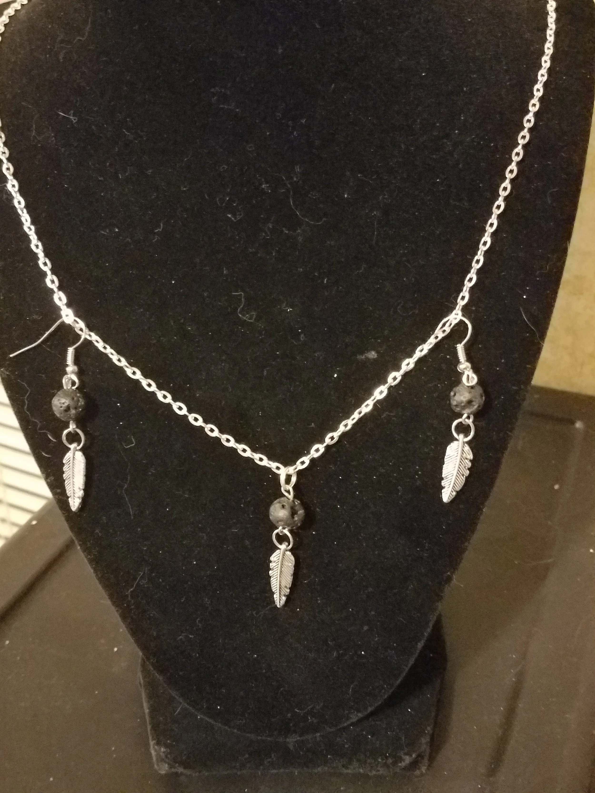 Silver necklace with three feather pendants and three black beads displayed on a black velvet bust.