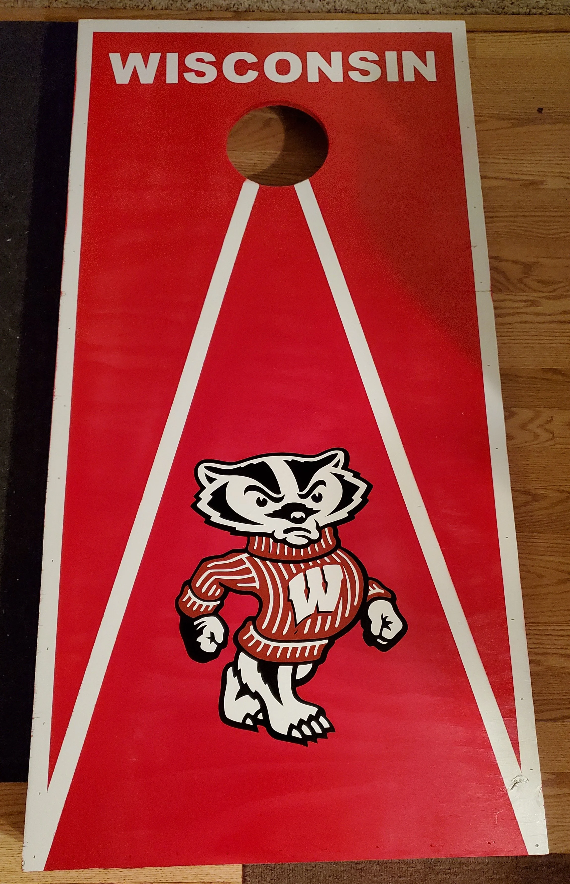Cornhole game board with Wisconsin Badgers mascot and team logo on a red background.