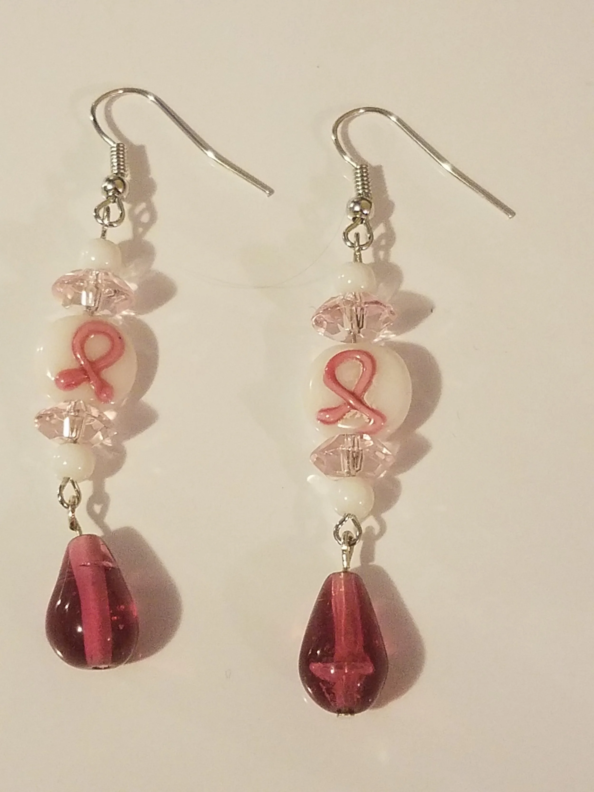 Pair of earrings with pink ribbons, pink and white beads, clear crystals, and red glass teardrop pendants.