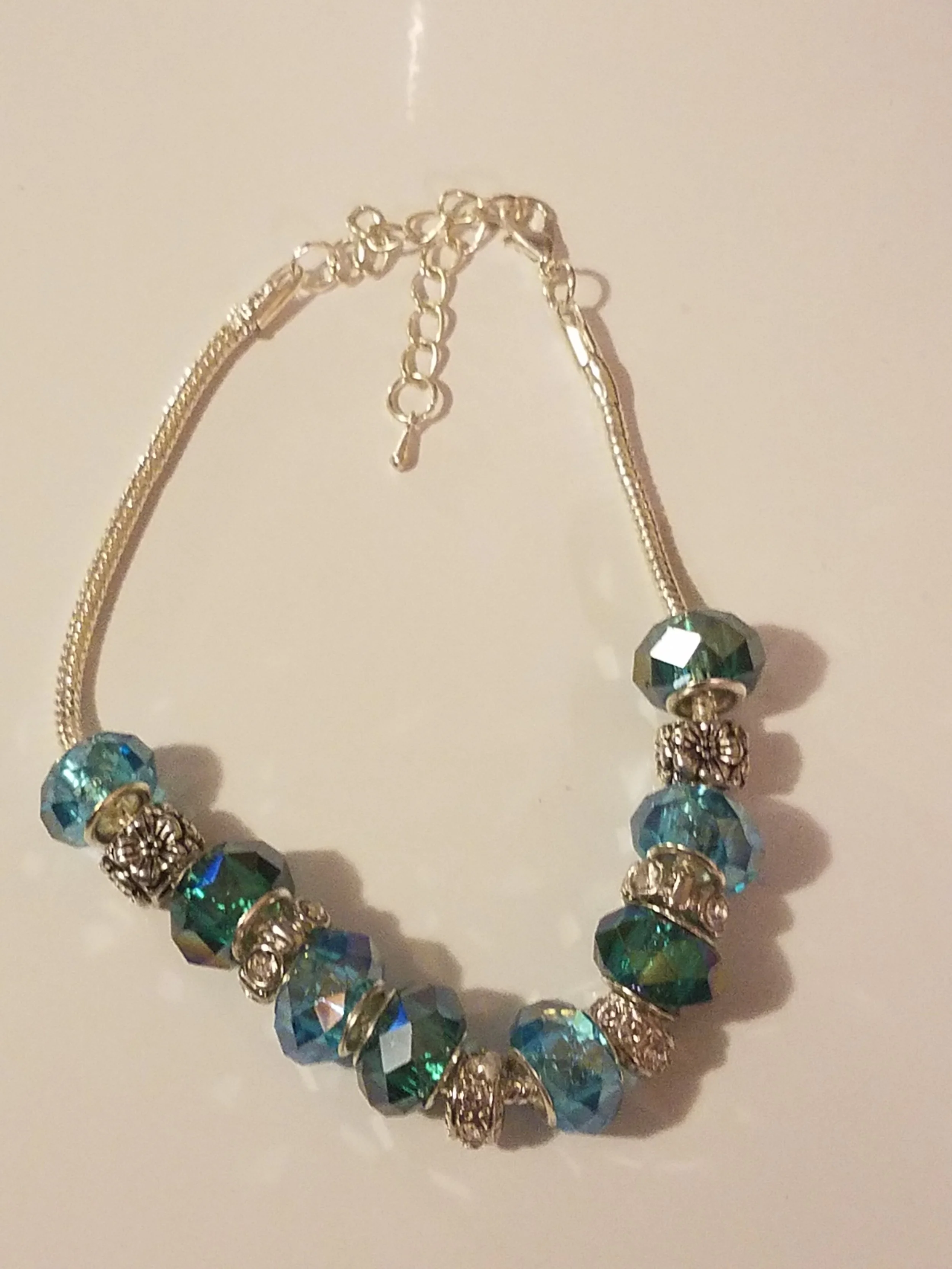 Silver bracelet with large faceted blue and green beads and decorative silver spacers.