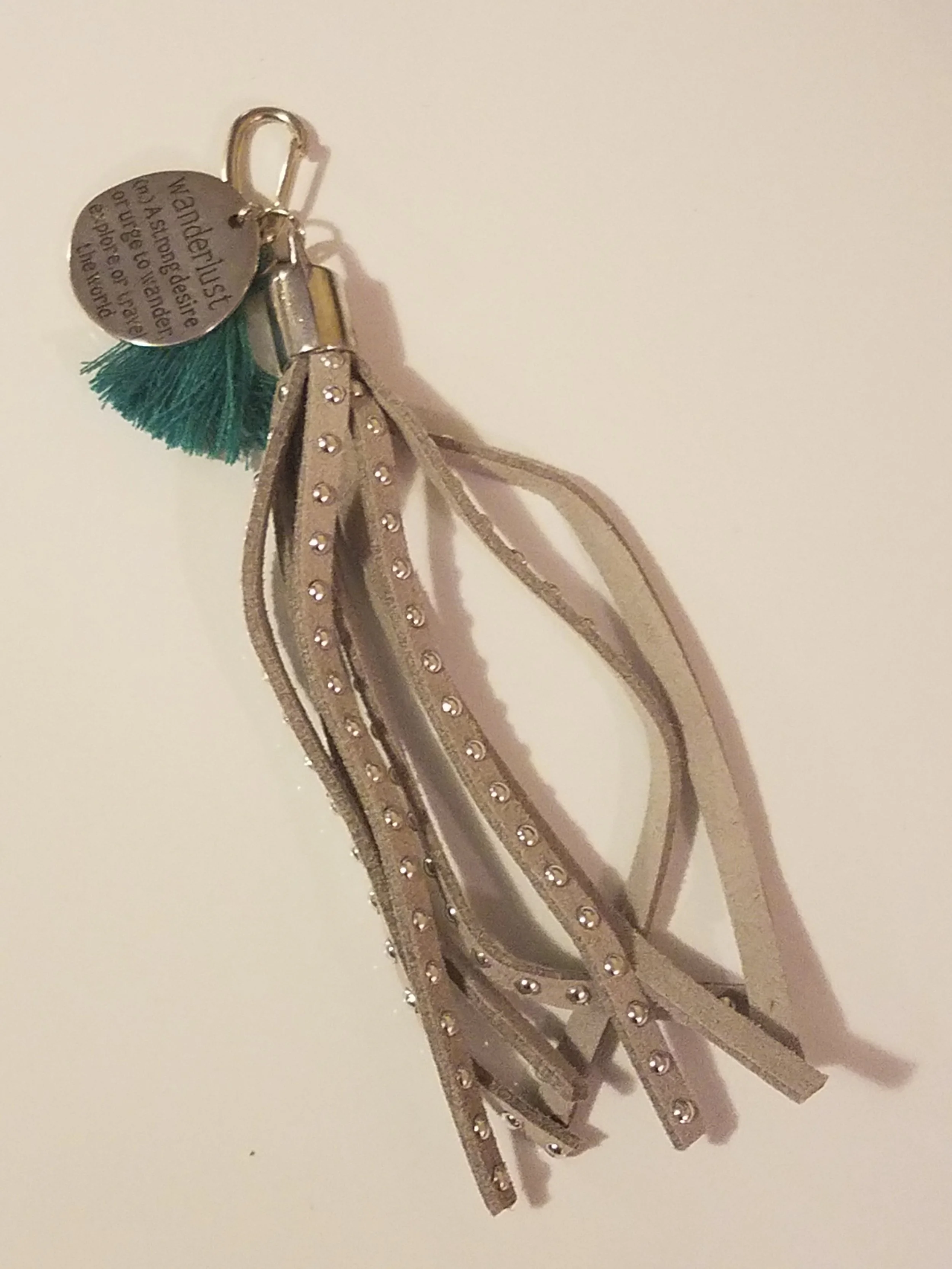 Keychain with a small green tassel, a metallic tag, and beige ribbons with rhinestones.