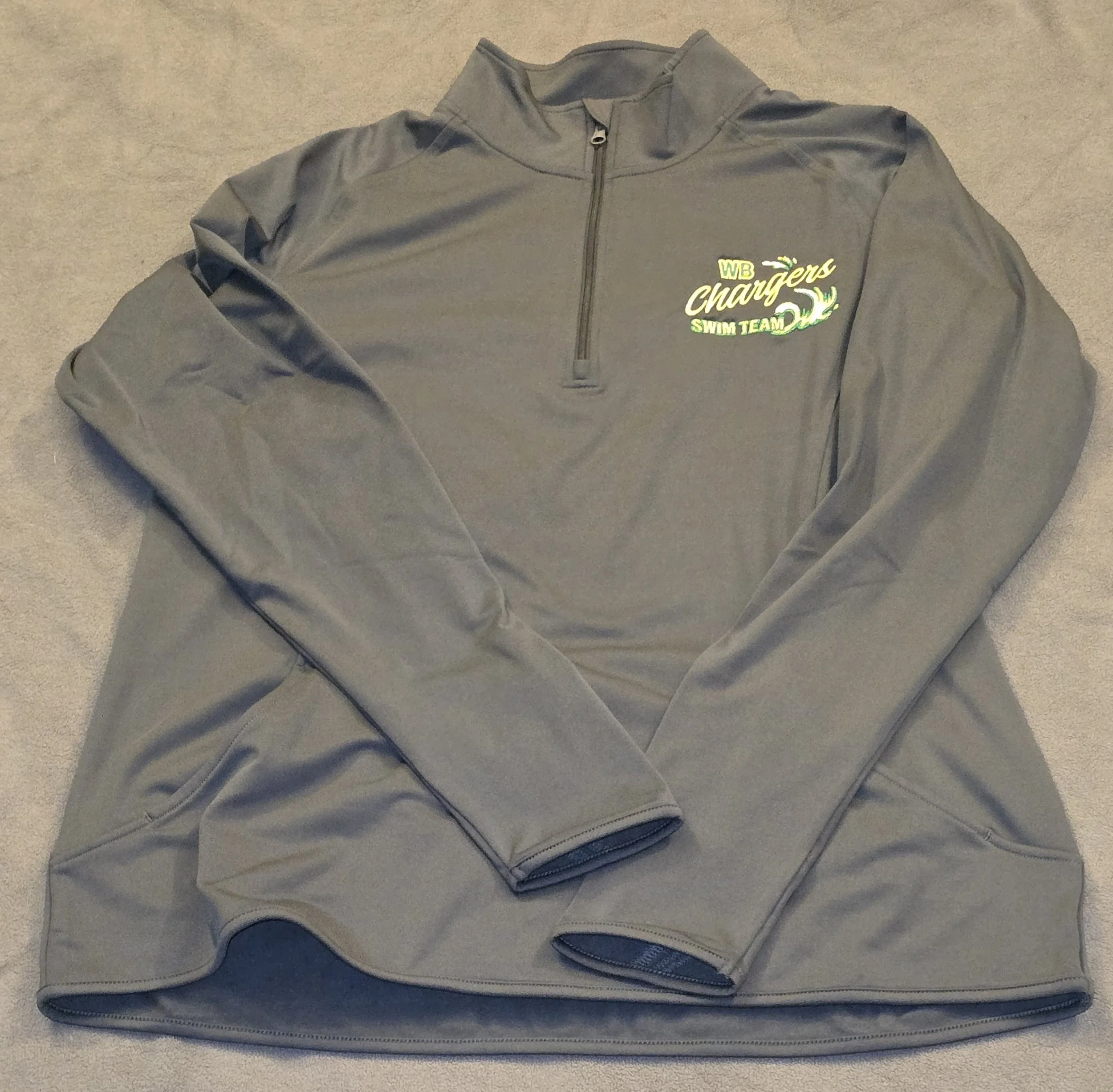 Gray half-zip sweatshirt with 'WB Chargers Swim Team' logo on the left chest area, lying on a beige carpet.