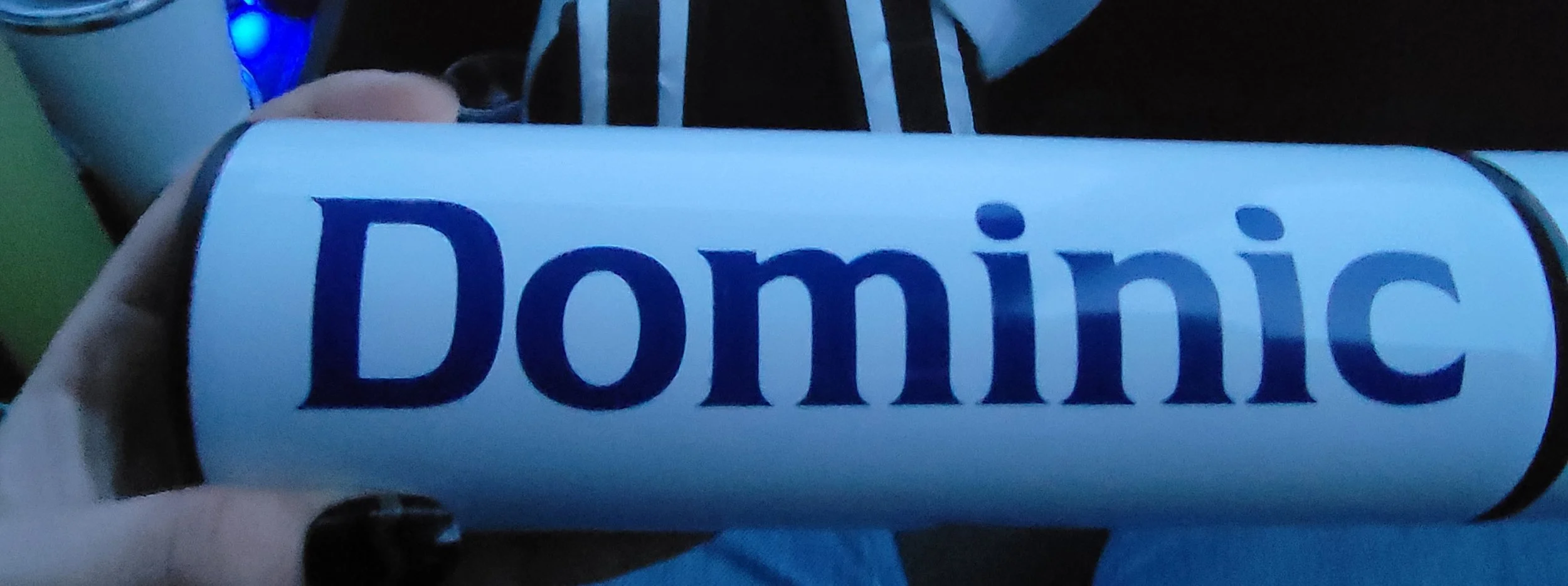 A person's hand holding a cylindrical container with the word 'Domino' printed on it, in a dark environment with blue lighting.