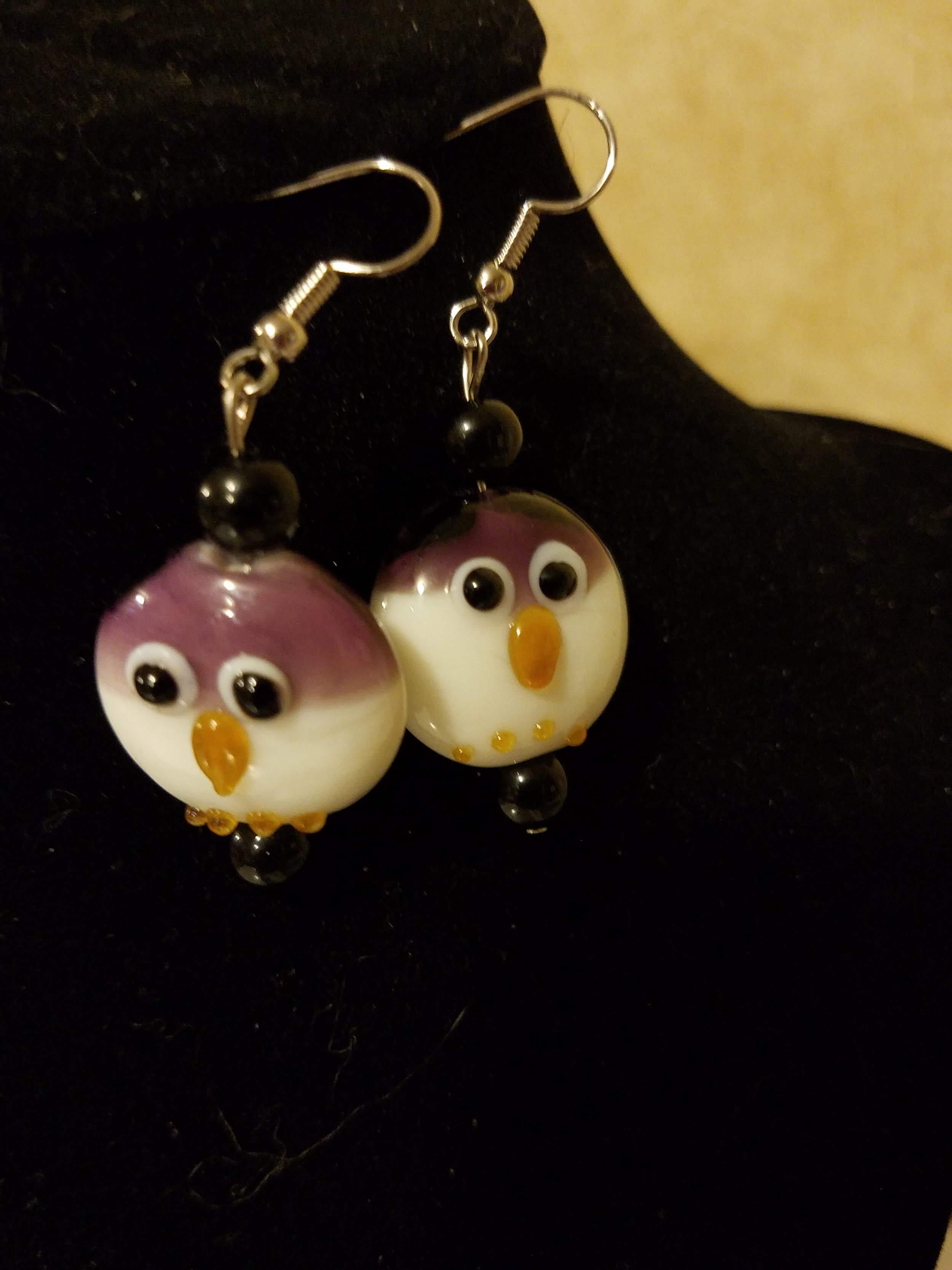 Pair of earrings shaped like cartoonish owls with large googly eyes, orange beaks, and colorful bodies, displayed on a black surface.